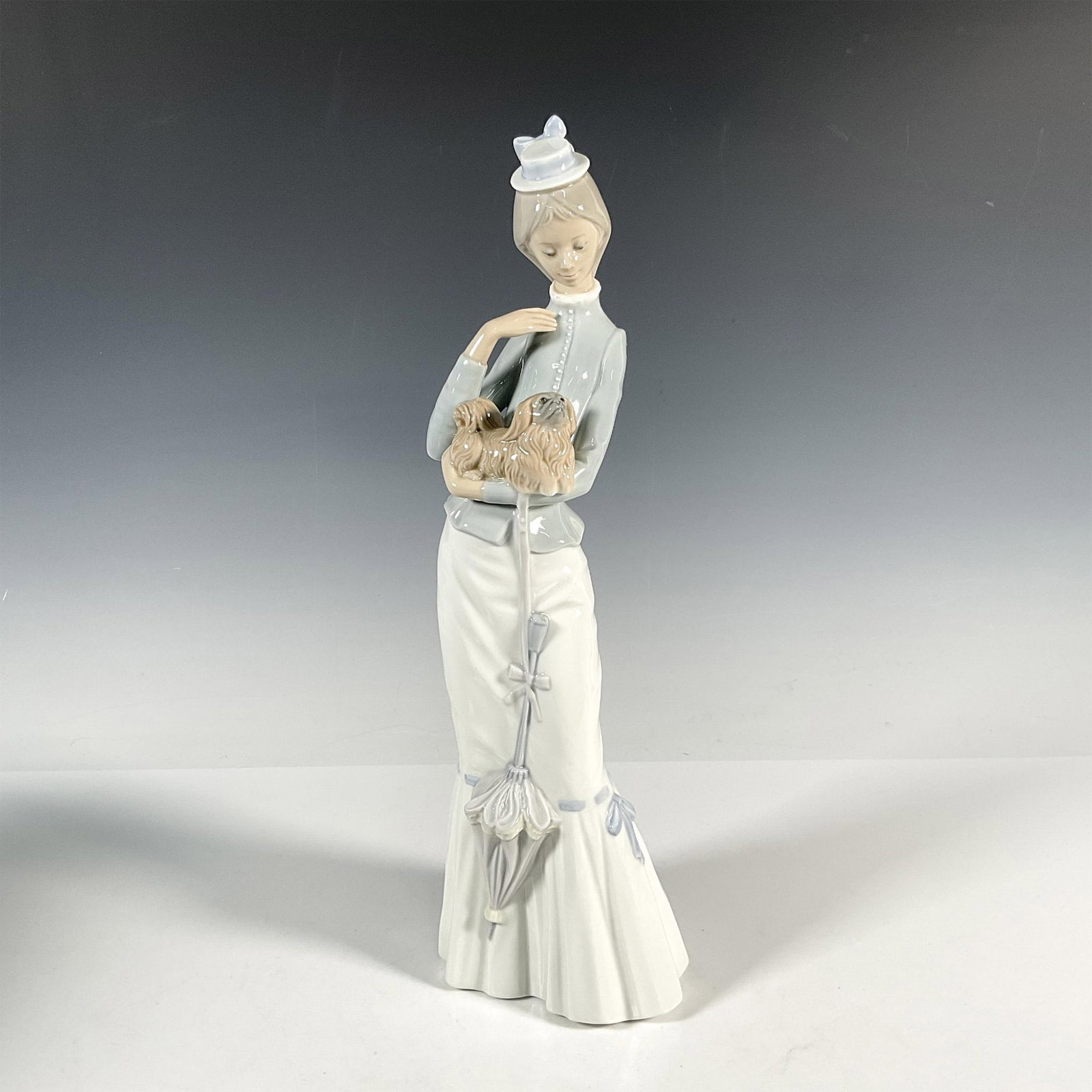 Walk With The Dog 1004893 - Lladro Porcelain Figurine: Glossy finish; Lladro backstamp. Includes original box: 17.75"L x 7"W x 6.5"H. Artist: Jose Roig Issued: 1974 - 2004 Dimensions: 15"H x 4.75"W Manufacturer: Lladro Country of Origin: Spain