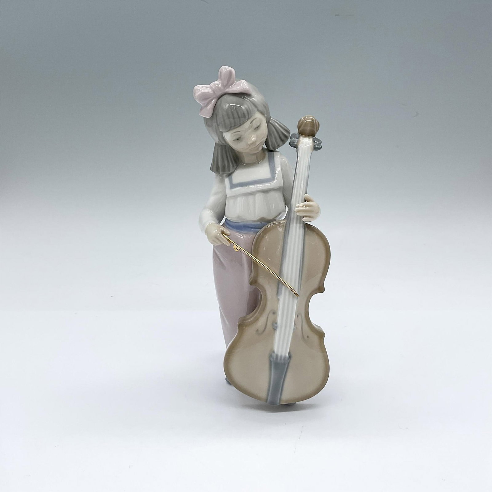 Nao by Lladro Porcelain Figurine, Girl With Cello 02001035: Glossy figure of a young girl playing the cello. Nao backstamp. This item has its original box: 9.25"L x 7.5"W x 6.5"H. Artist: Francisco Catala Issued: 1992 Dimensions: 3.25"L x 3"W x 7.5"H Manufactu