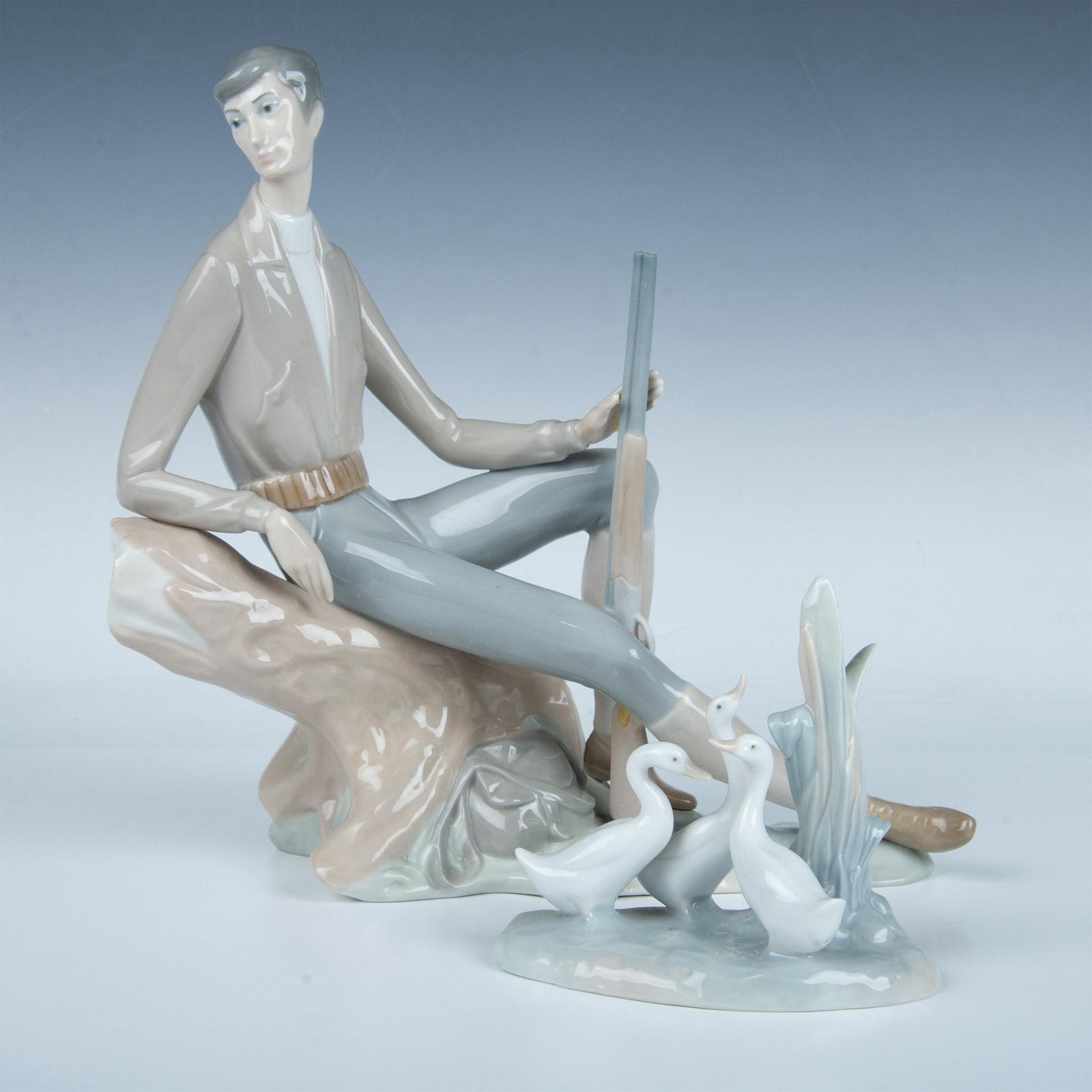 2pc Nao by Lladro Porcelain Figurines, Hunter and Ducks: Two glossy figures, one of a hunter resting with a rifle and the other is a group of ducks. Nao backstamps. Hunter: 11.25"L x 4.75"W x 10.75"H. Ducks: 5"L x 2.75"W x 4.5"H. Dimensions: See Description