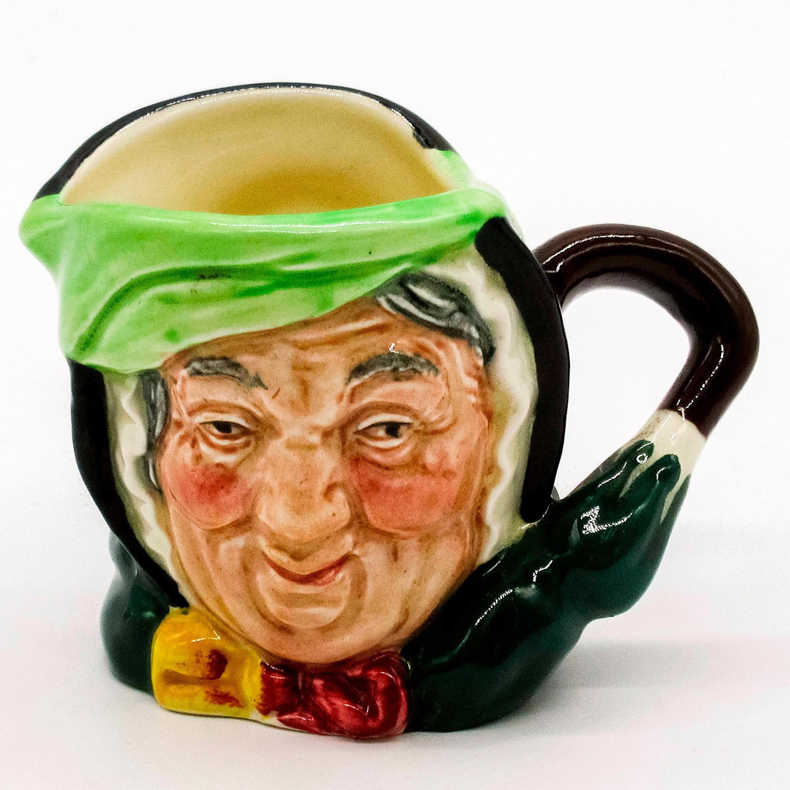 Sairey Gamp D6045 - Mini - Royal Doulton Character Jug: Black hair; light green band; dark green coat; yellow and burgundy bow. Royal Doulton backstamp. Good condition. #royaldoulton #characterjug #saireygamp Artist: Leslie Harradine and Harry Fenton Issue