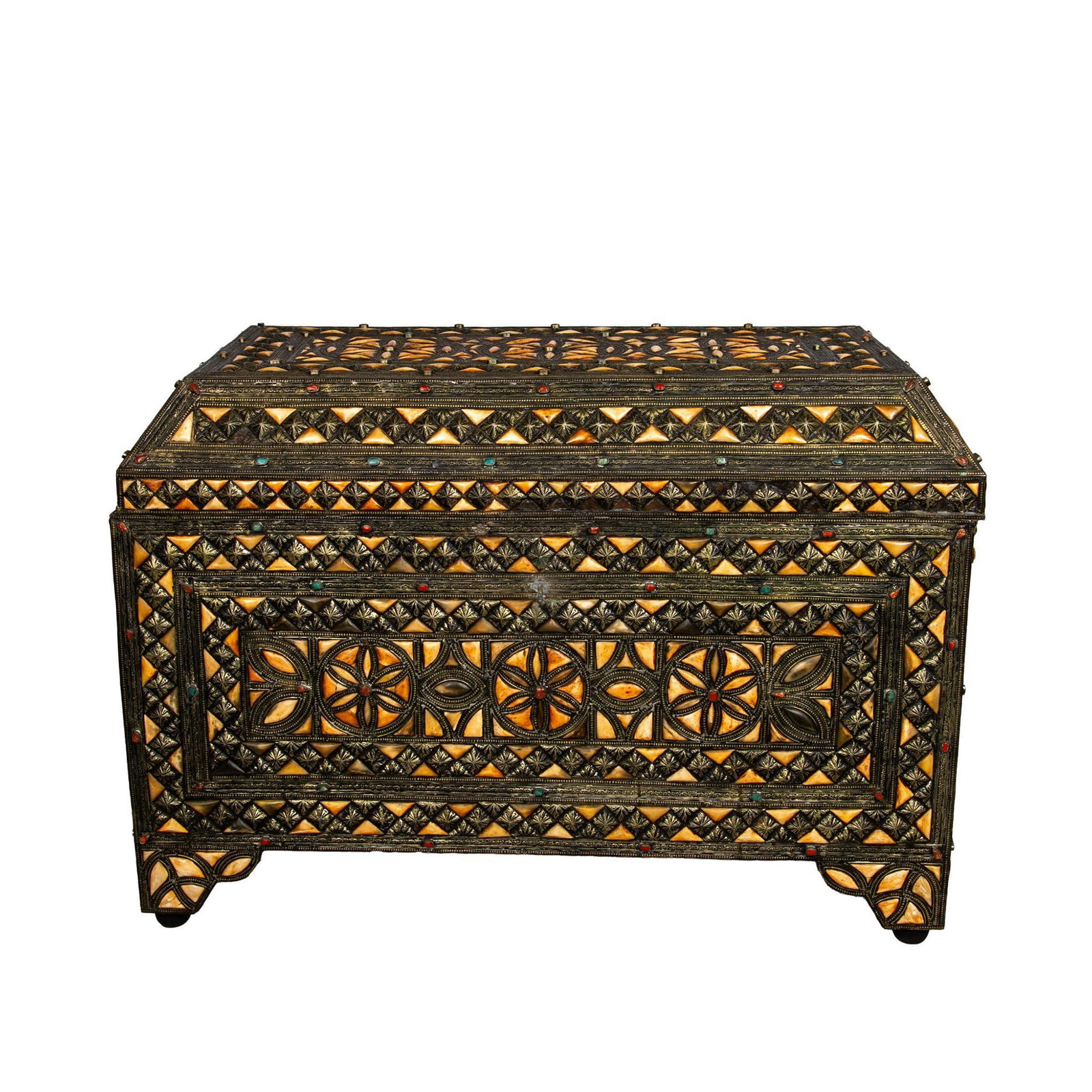 Moroccan Style Bone Inlaid Wooden Chest: A footed storage chest ornately adorned with bone fragments carved and organized in a floral pattern. Accented with blue and red stones, and intricate embossed patterned metal lining. A handwoven clot