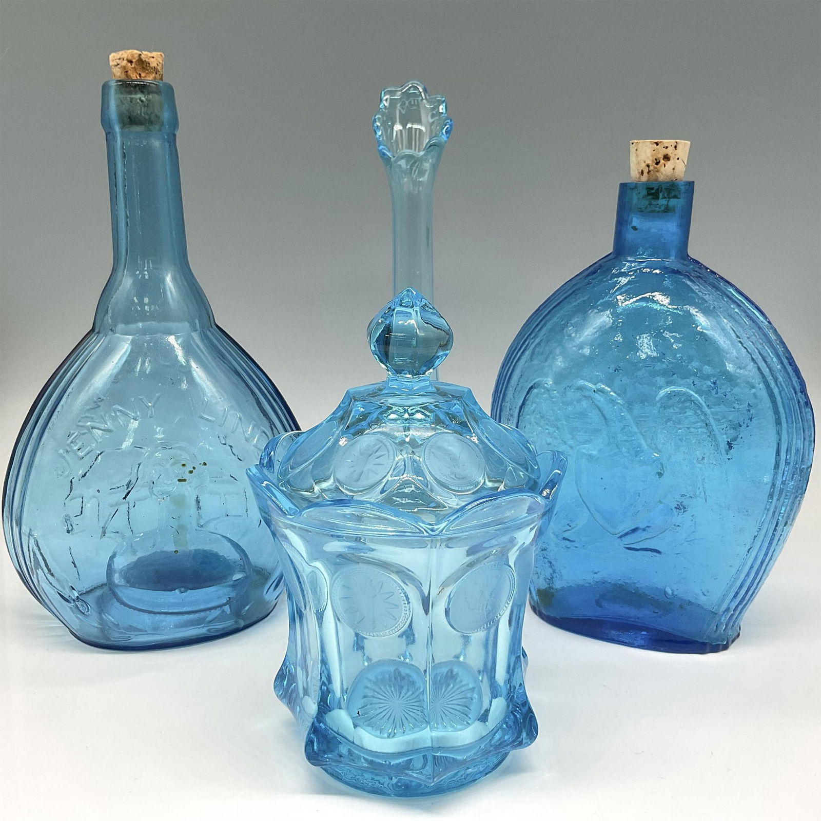 4pc Blue Glass Group including Empire, Fostoria & Clevenger: Cornflower blue glass bottles - Jenny Lind molded bust design on front from Empire Glassworks, flask bottle with molded eagle design on front from Clevenger Bros. Glassworks, glass bud vase and Fostor