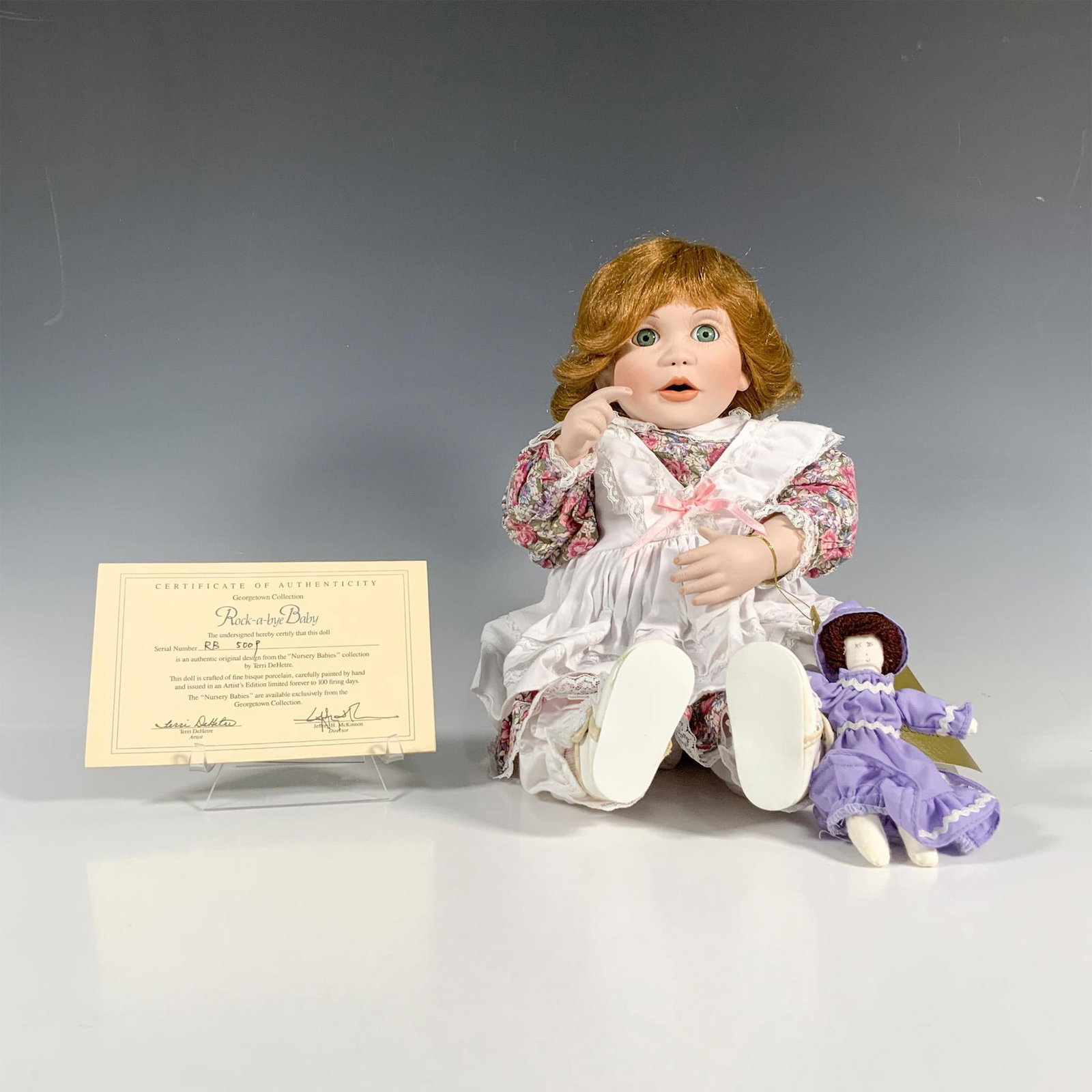 Georgetown Collection Nursery Babies Doll, Rock-a-Bye Baby: Discover the Georgetown Collection Nursery Babies Doll, Rock-a-Bye Baby, featuring a baby doll with red hair, green eyes, a floral dress, and white apron. This set includes a smaller companion doll in