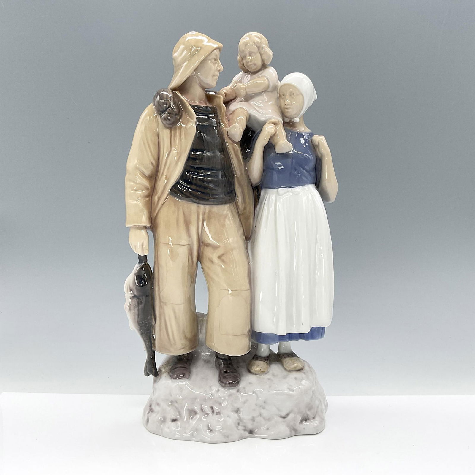 Bing and Grondahl Figurine, Fisherman Family 2025: This impressive figurine depicts a fisherman's family, with the adults holding their small child on their shoulders. Finished in glossy underglaze technique with subtle hues of blue, white, and grey.
