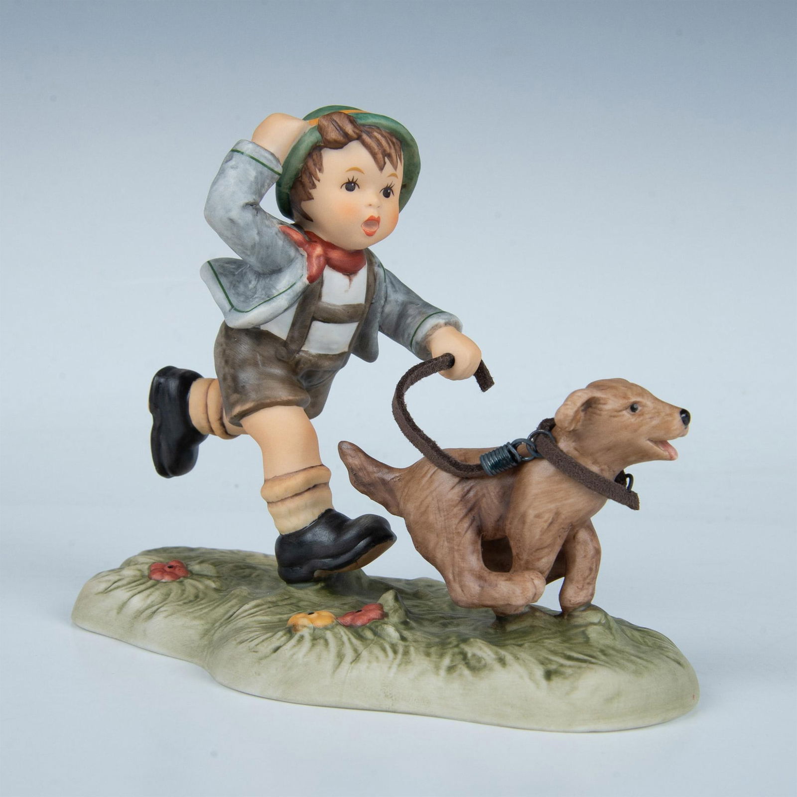 Goebel Hummel Figurine, Carried Away: Matte painted boy running after his dog on a leash. Goebel backstamp. Artist: Berta Hummel Issued: 20th c. Dimensions: 6"L x 3"W x 4.5"H Manufacturer: Goebel Hummel Country of Origin: Germany