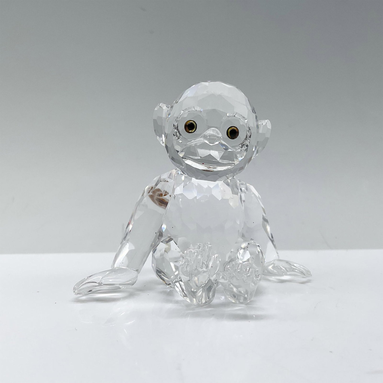 Swarovski Crystal Figurine, Chimpanzee 221625: A clear crystal figure depicting a young chimpanzee that is sitting on his bottom with his arms outstretched. Swarovski backstamp. Includes a Swarovski box. Dimensions of box: 5.5"H x 6" dia. Artist: 