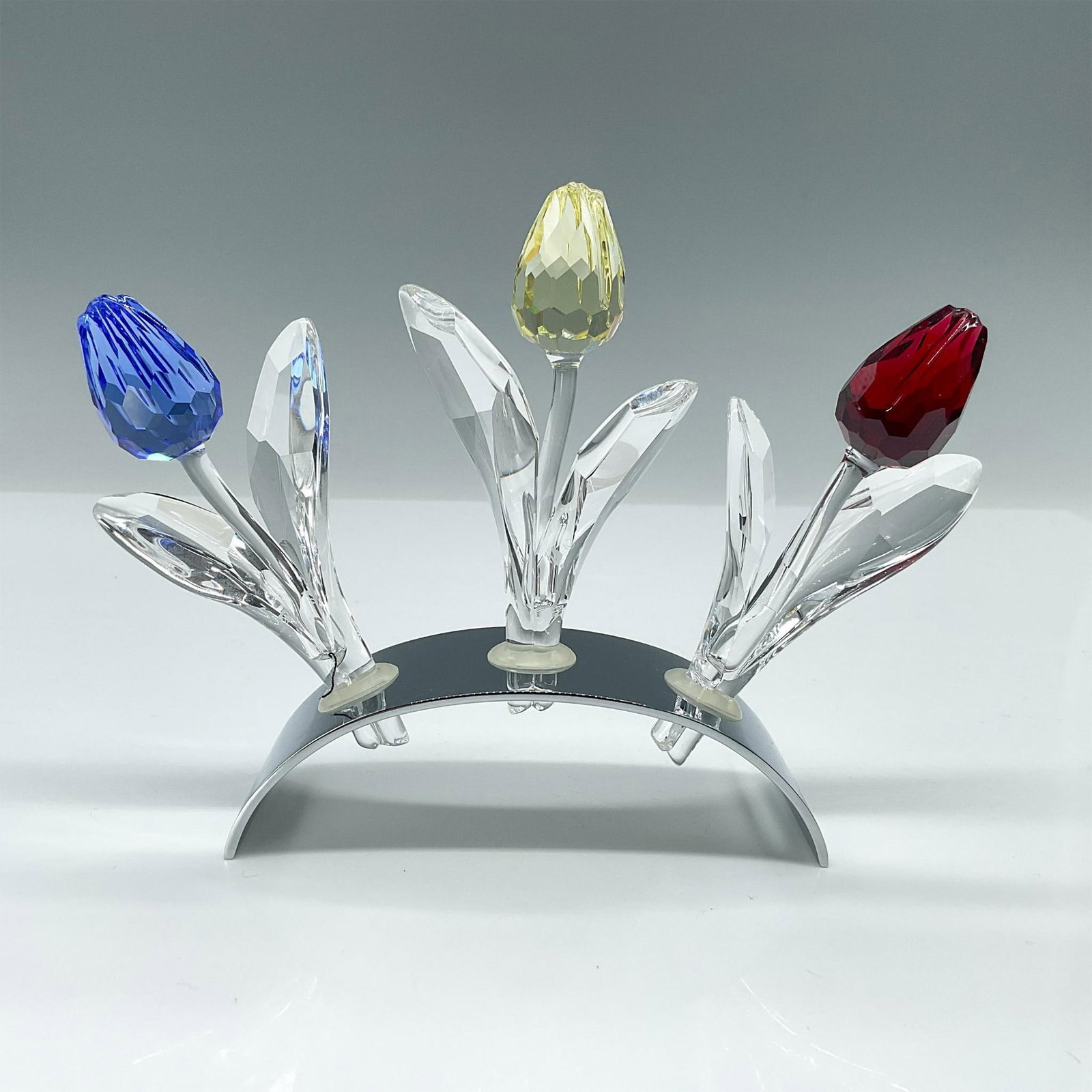 4pc Swarovski Crystal Figurine, Crystal Tulips with Holder: Three beautiful flowers in blue, yellow, and red, presented in a mirrored holder. Swarovski backstamp. Issued: 2002-2004 Dimensions: 6.25"L x 1.5"W x 4.25"H Manufacturer: Swarovski Country of Origin: 