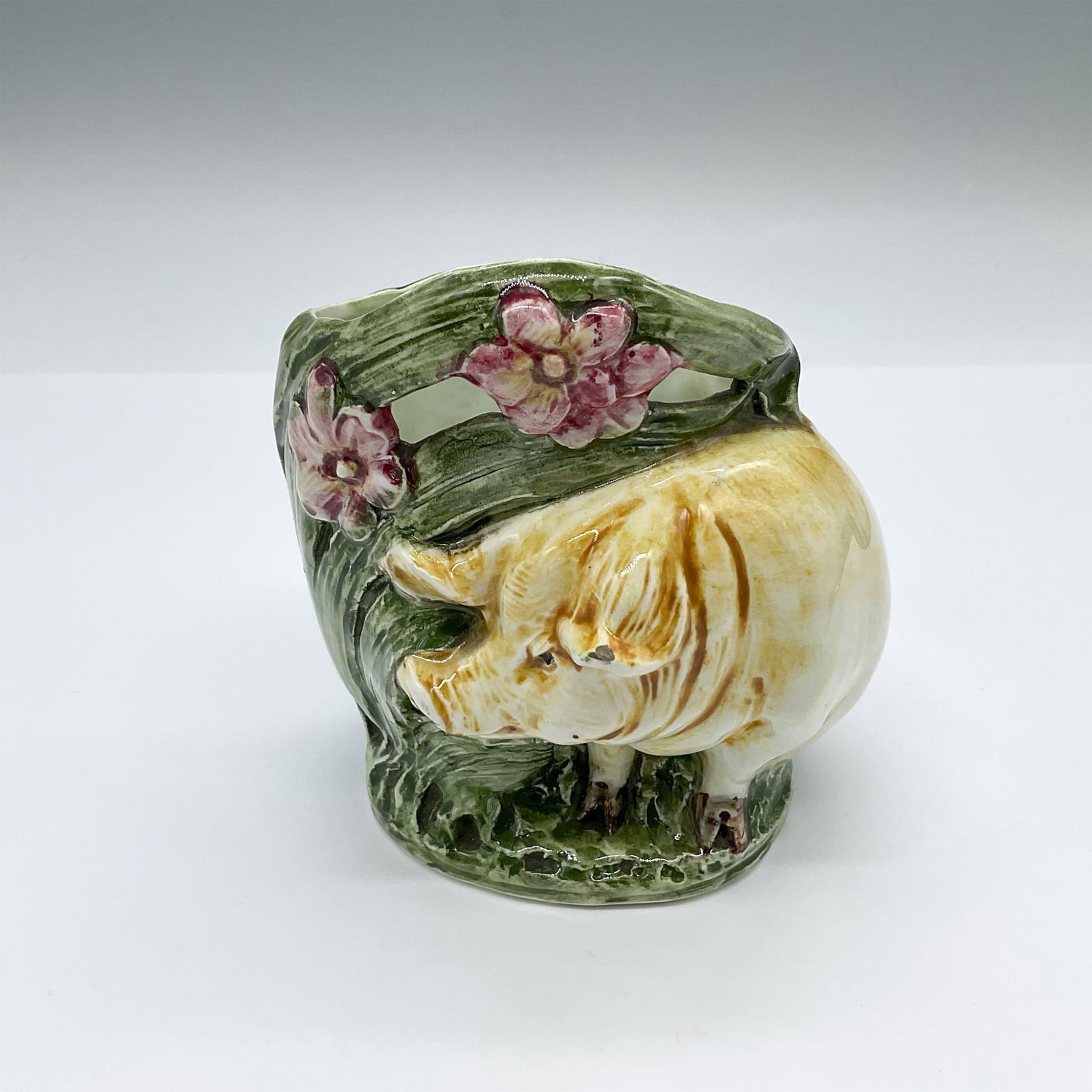 Majolica Pottery Pig Vase: Hand made and hand decorated vessel featuring a rotund pig seated by a bush with pink flowers. 8483 impressed on the underside. Dimensions: 4.25"L x 3.75"W x 4.5"H