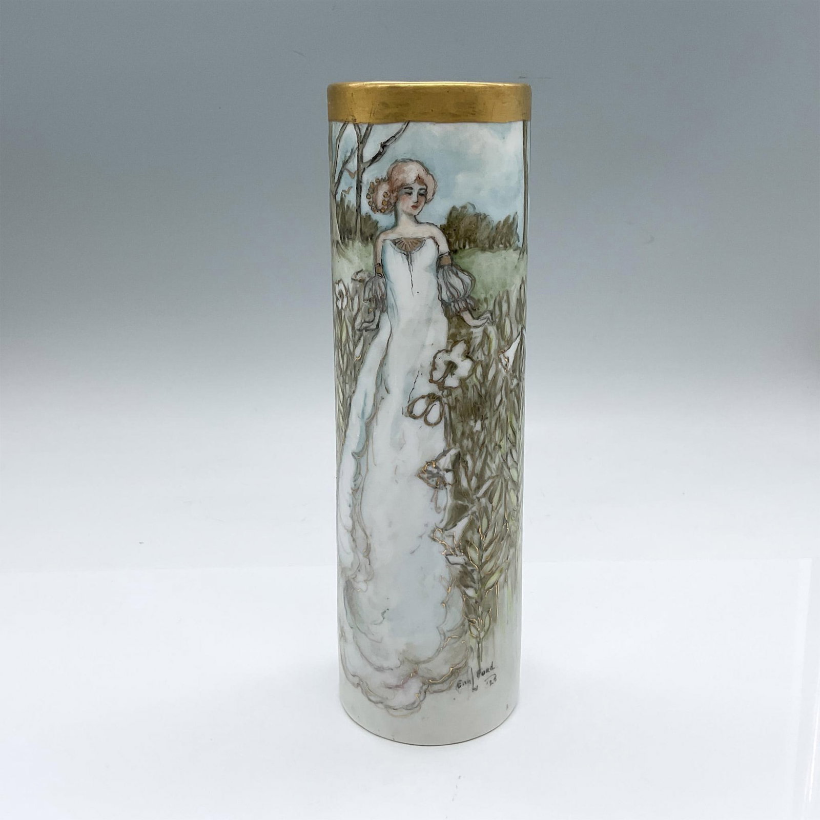 Jaeger by E. Ford German Porcelain Vase, Signed: Hand painted cylindrical vase a gilt band at the top, and depicts a woman standing in a field of flowers. Gold paint outlines the flowers. Jaeger backstamp. Artist signed on the lower bottom. Artist: 