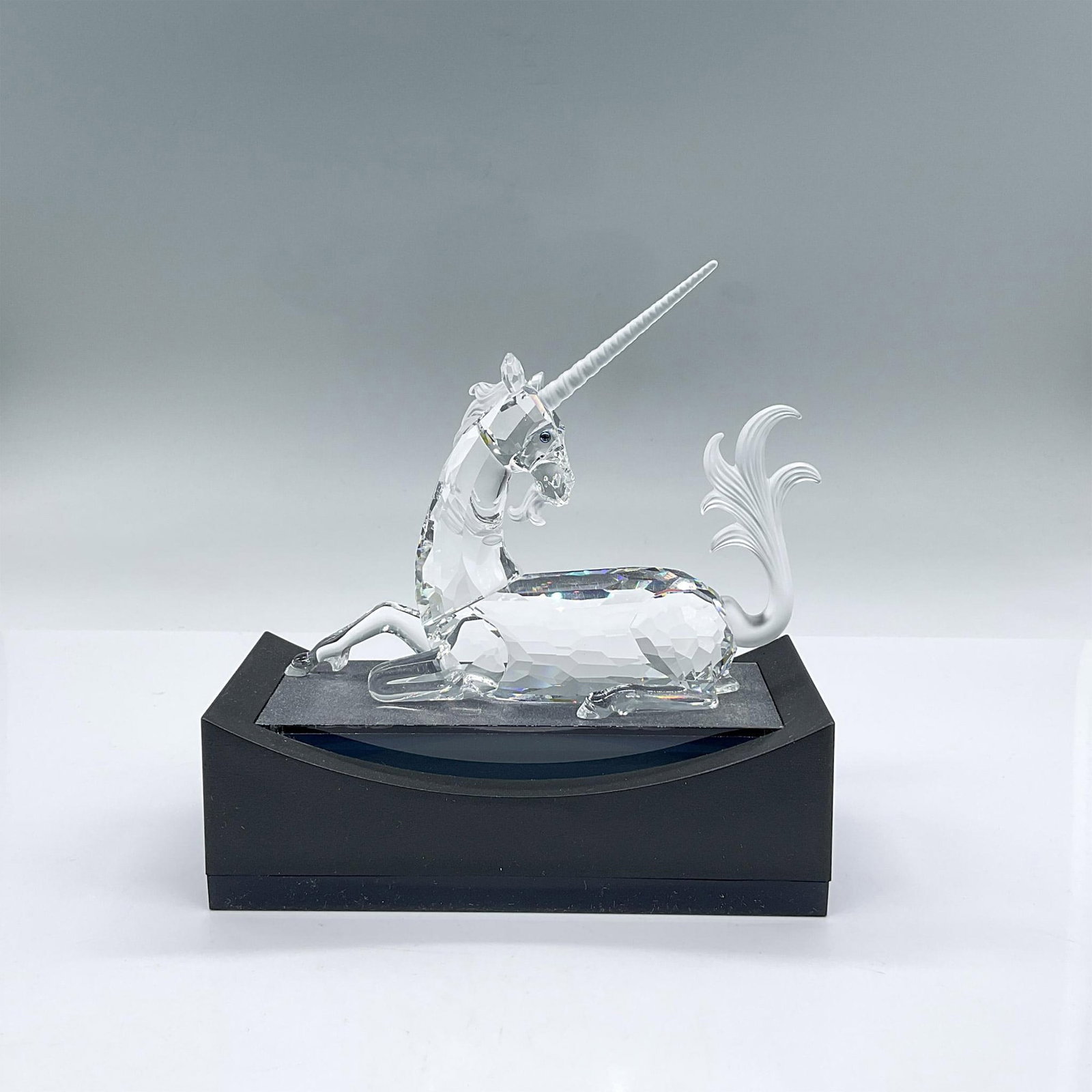 Swarovski Crystal Figurine, The Unicorn + Base: Brilliant faceted crystal figure of a majestic unicorn lying down with frosted horn, tail and mane. Swarovski etched mark. The Unicorn was the first of the Fabulous Creatures trilogy. Includes stand 6