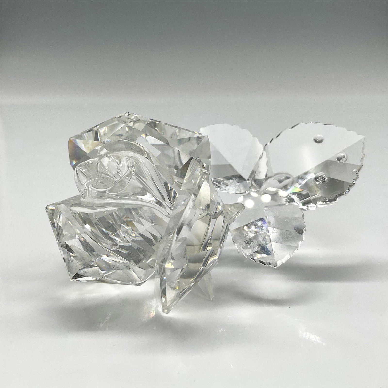 Swarovski Crystal Figurine, Rose Blossom: Clear crystal of flower opening with crystal rhinestones as water drops. Swarovski backstamp. 890289. Artist: Elisabeth Adamer Issued: 2007 - 2013 Dimensions: 1.75"L x 3"W x 1.75"H Manufacturer: Swaro
