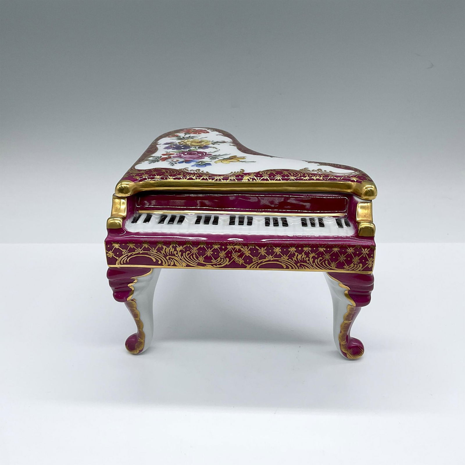 Castel Porcelain Limoges French Piano Box: Hand made cover decorative box in a shape of a grand piano. Dark maroon with hand painted flowers and gilt gold swirls. Castle backstamp. Issued: c. 1945-1967 Dimensions: 6.25"L x 5.75"W x 4.25"H Manu