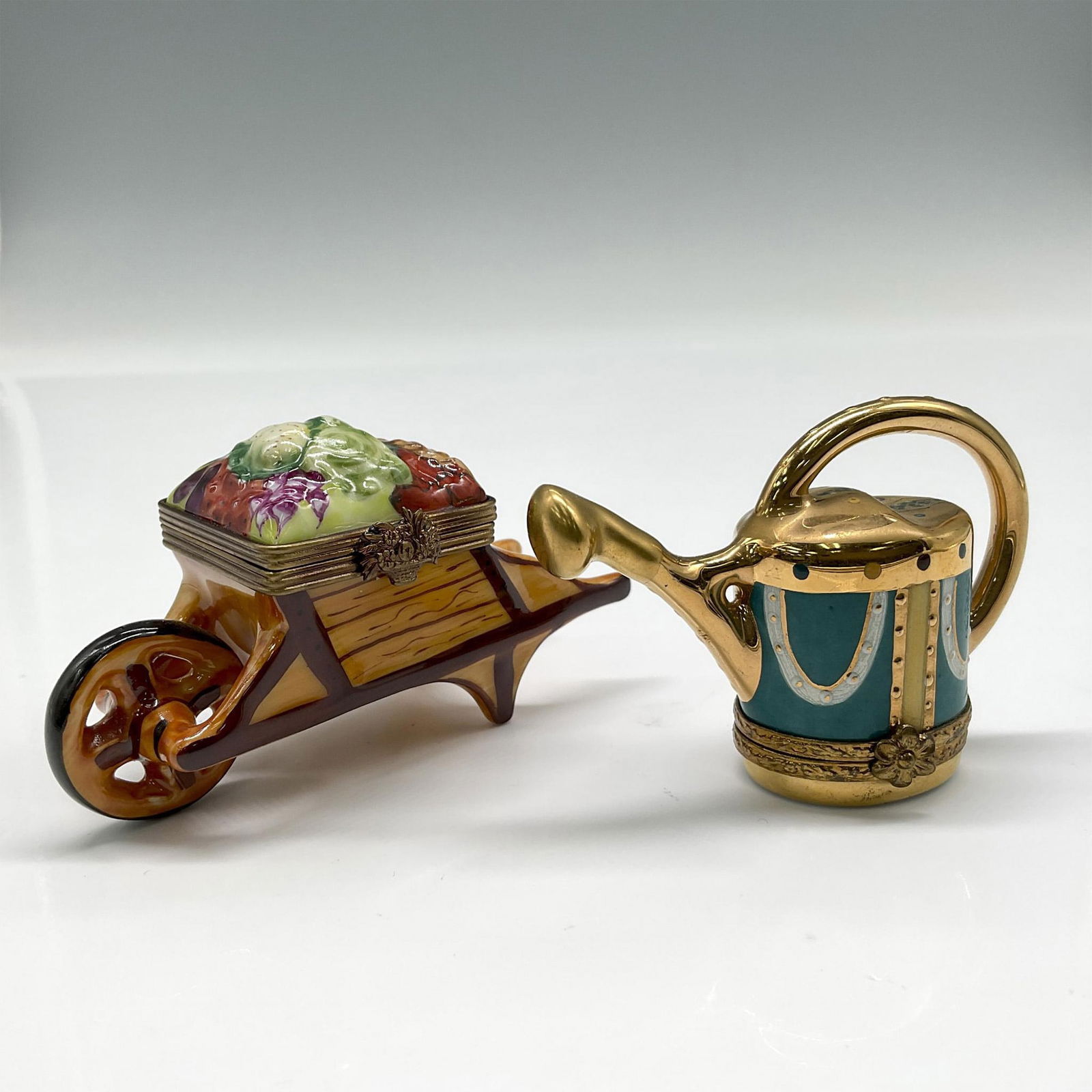 2pc Limoges Porcelain Wheelbarrow & Watering Can Pill Boxes: Lot includes wheelbarrow with colorful flowers 2"H and gilt watering can 2"H over green coloration. Limoges backstamp. Largest piece: 3.25"L x 1.25"W x 2"H. Issued: 20th century Dimensions: See Descri