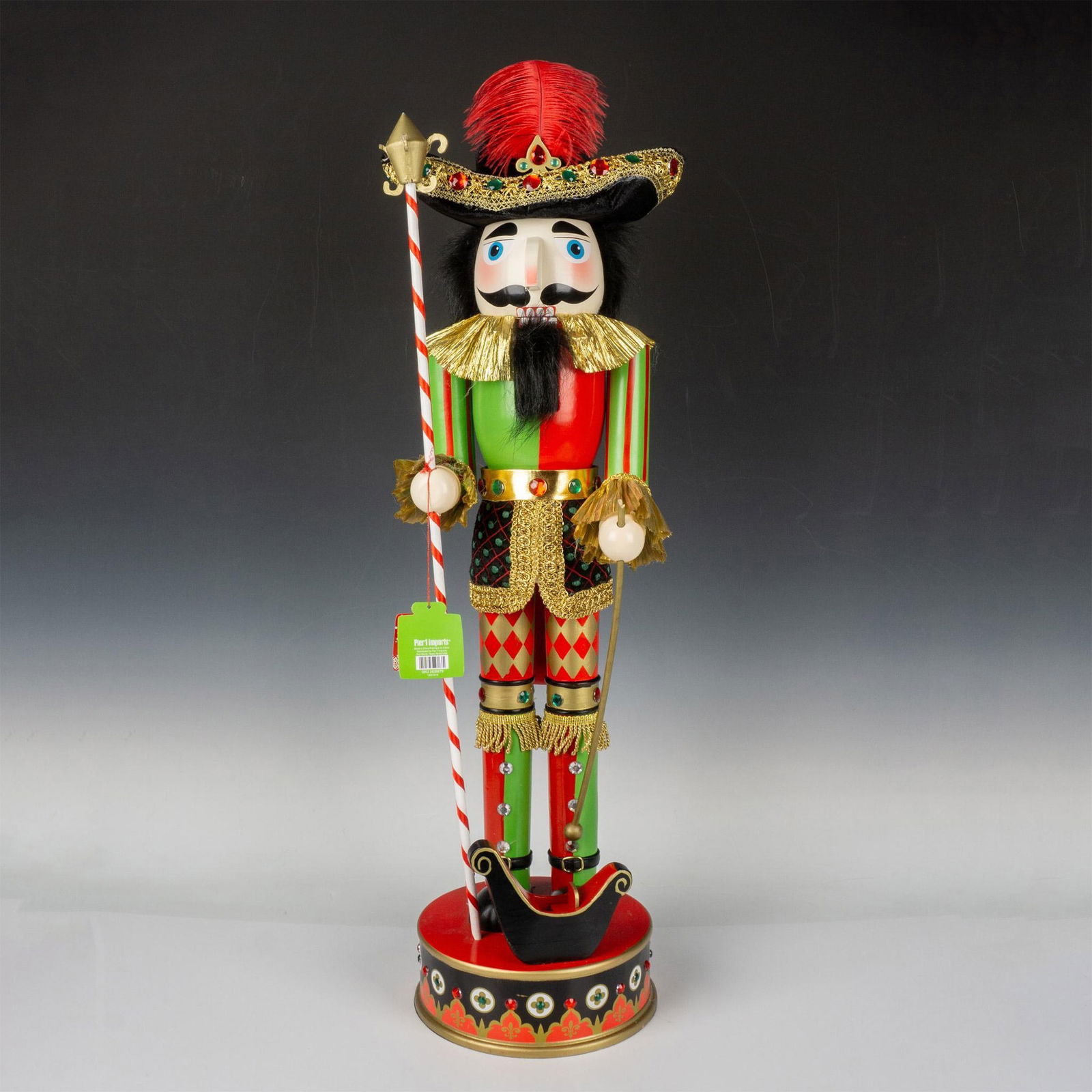 Pier 1 Imports 2012 Collection Tall Nutcracker: A nutcracker, dressed as a gallant soldier in vibrant red, green, and black attire, wielding a spear atop a matching base. Pier 1 Imports manufacturing tag. Issued: 2012 Dimensions: 33.5"H x 8.75" dia