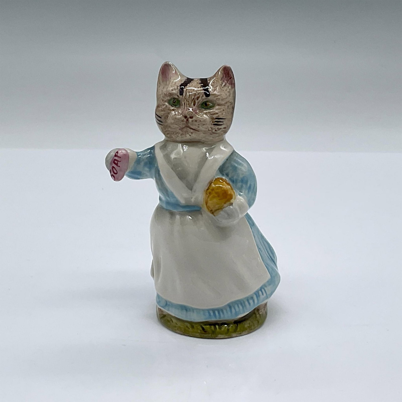 Beswick Beatrix Potter Figurine, Tabitha Twitchit: Modeled with white V neck to her dress and holding a bar of pink soap. Beswick backstamp. Issued: 20th c Dimensions: 2.5"L x 2"W x 3.5"H Manufacturer: Beswick Country of Origin: England