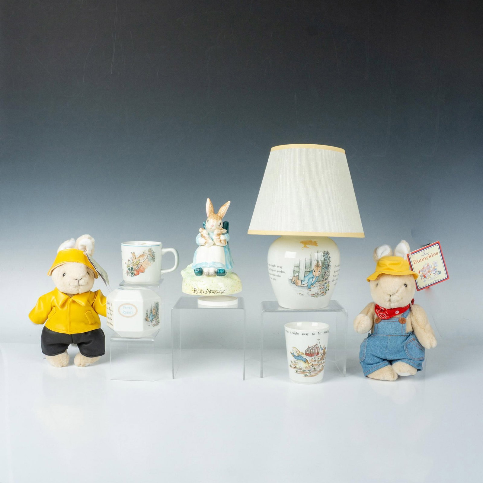 7pc Wedgwood Peter Rabbit Lamp/Bank/Mug/Cup/Plush Bunnies: Cheerful group of decorative Bunnykins items. Wedgewood bone china, stamped. Mug and cup. Lamp with shade 12.25"H x 8" dia. Hexagon shaped coin bank 3.75"L x 3.25"W x 3.25"H. Schmid Mrs. Rabbit music
