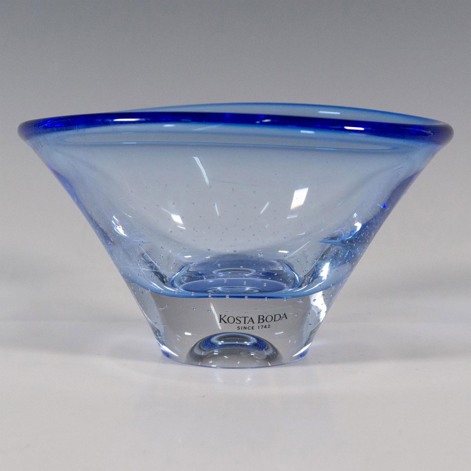 Kosta Boda by Goran Warff Blue Glass Bowl, Zoom Signed: A small translucent conical oval formed bowl decorated with controlled air bubbles. Kosta Boda marked. Artist signed on the underside. Artist: Goran Warff Dimensions: 4.75"L x 4.25"W x 2.75"H Manufact