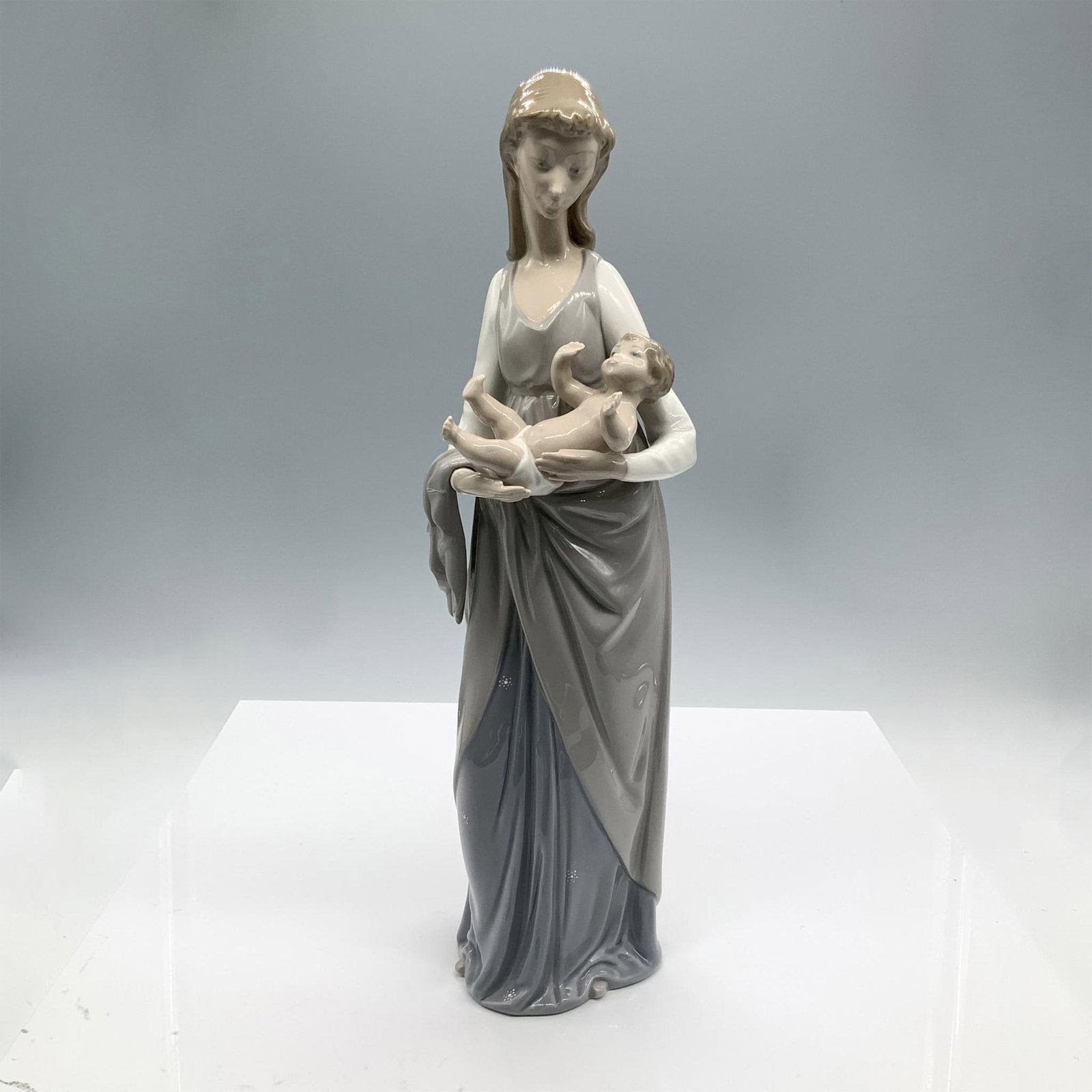 Mother and Child 1005086 - Lladro Porcelain Figurine: A mother holding a child boy in her arms. Lladro backstamp. Artist: Vincente Martinez Issued: 1980-1983 Dimensions: 4.5"L x 5"W x 15.5"H Manufacturer: Lladro Country of Origin: Spain