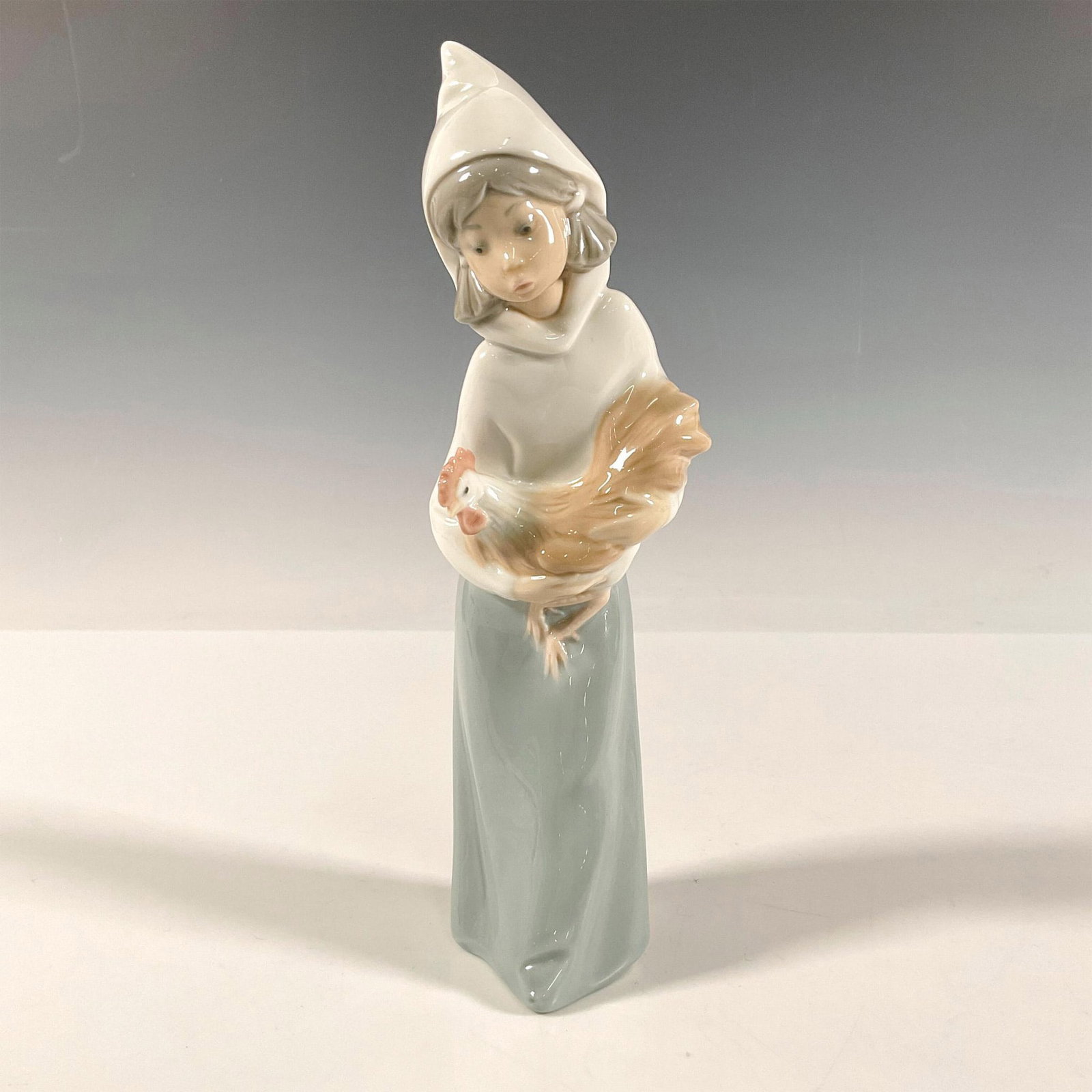 Girl Holding Rooster 1004677 - Lladro Porcelain Figurine: Figure of a young girl carrying a rooster to an unspecified location. Glossy finish. Lladro backstamp. Artist: Juan Huerta Issued: 1969-2001 Dimensions: 2.75"L x 2.75"W x 7.75"H Manufacturer: Lladro C