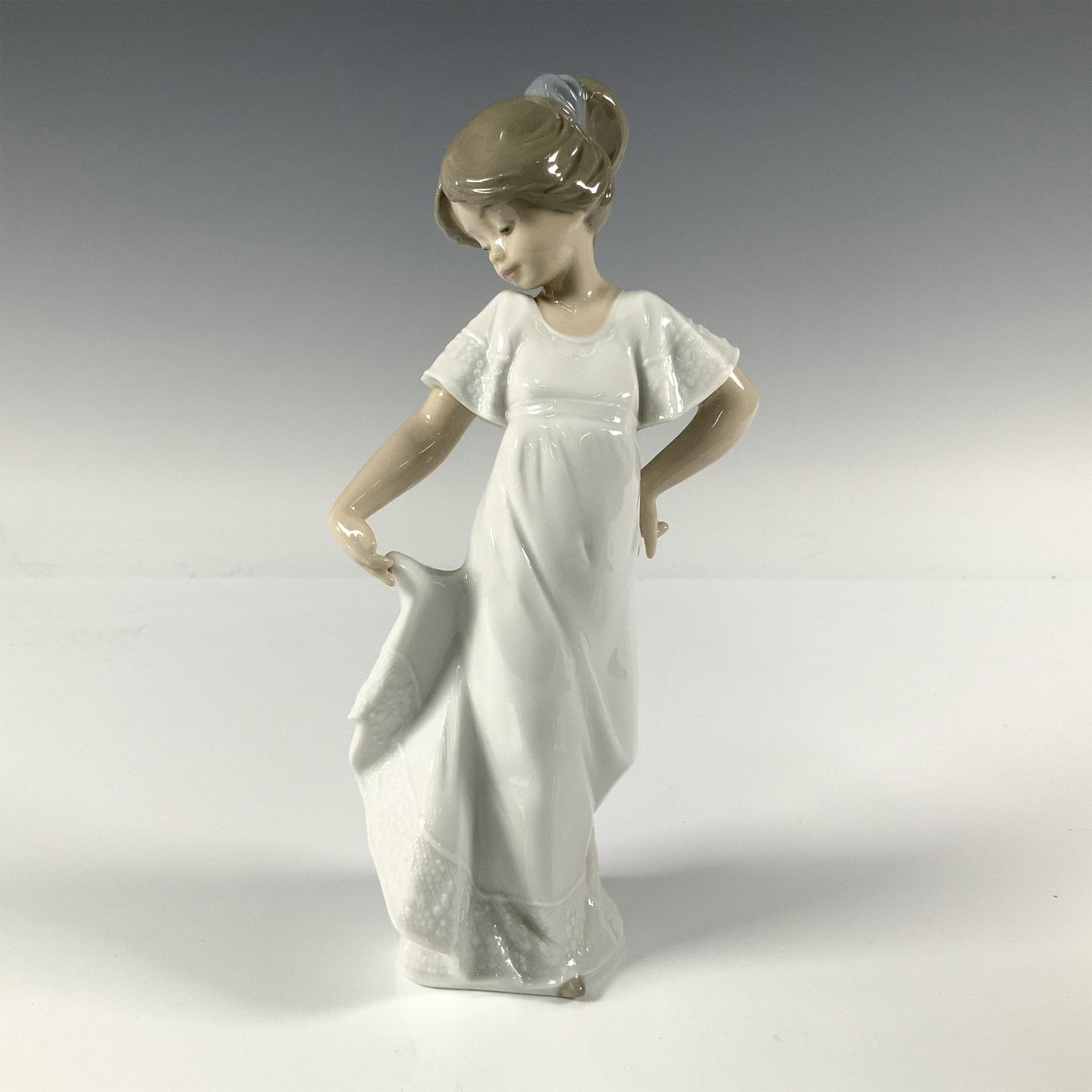 How Pretty! 2001110 - Nao By Lladro Porcelain Figurine: A figurine of a young girl, dressed in white, as she playfully lifts the end of her dress. Nao by Lladro backstamp. Artist: Antonio Ramos Issued: 1992 Dimensions: 4"L x 3.25"W x 9"H Manufacturer: Nao 
