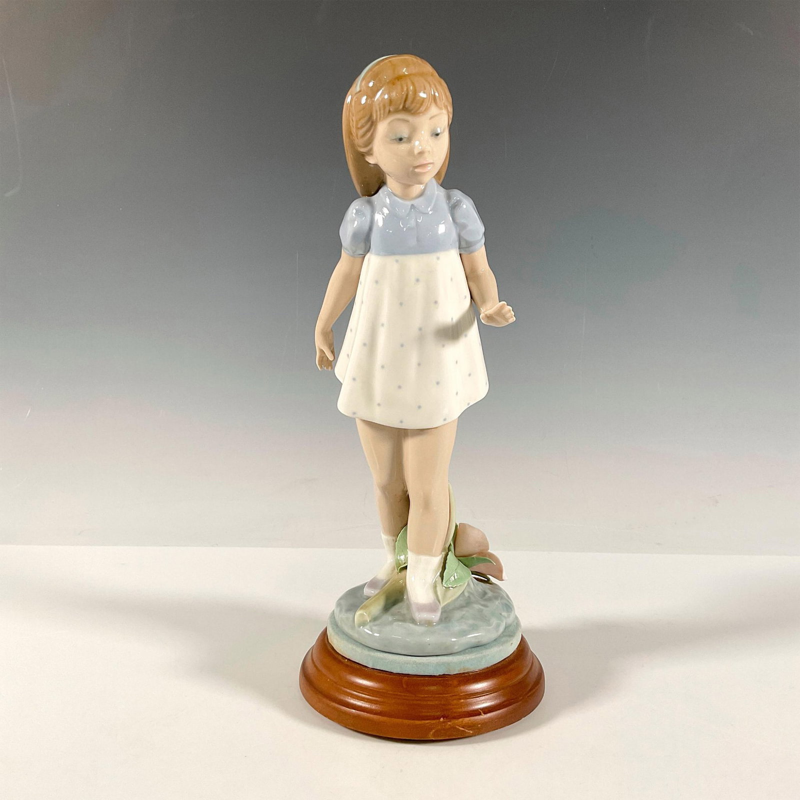 Lladro Porcelain Figurine, Girl Walking 1005040 + Base: Figure of a young girl stepping over a pink flower. Glossy finish. Lladro backstamp. This item has a base included that measures 1.25"H x 4.5" dia. Artist: Francisco Catala Issued: 1980-1981 Dimension