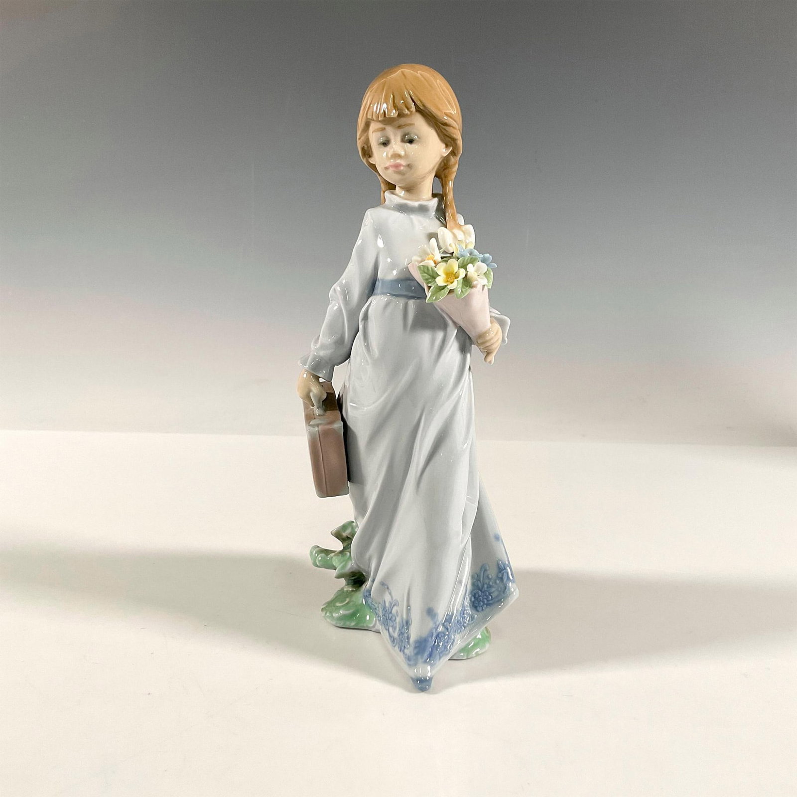 School Days 1007604 - Lladro Porcelain Figurine: Glazed figure of a young girl with braids carrying a suitcase. Artist signature. Lladro backstamp. Artist: Antonio Ramos Issued: 1988 Dimensions: 2.5"L x 4.25"W x 8.25"H Manufacturer: Lladro Country o