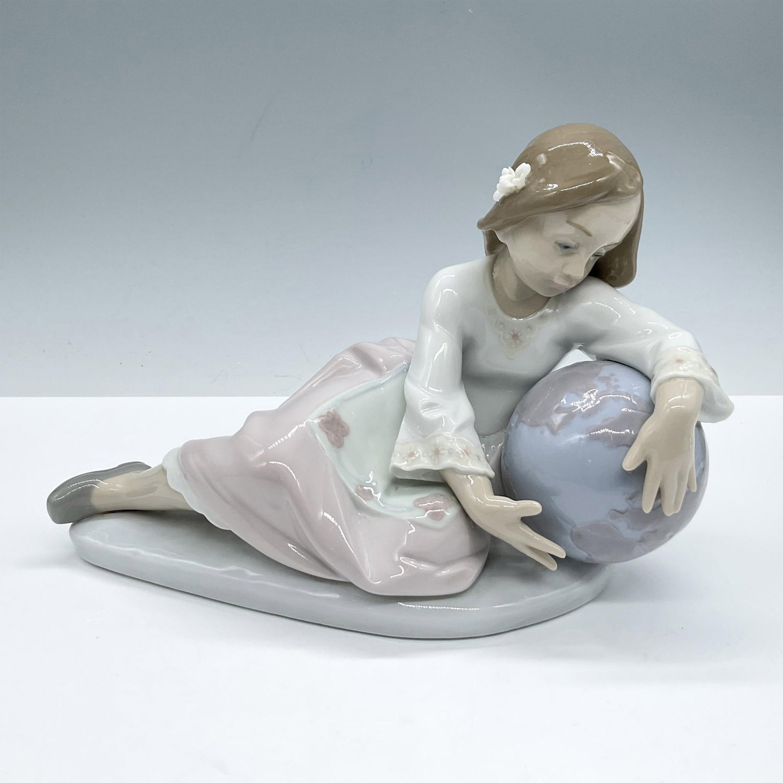 World of Fantasy 1005943 - Lladro Porcelain Figurine: Glossy finish, presents a girl dressed a embroidery dress laying admiring a world globe, Lladro backstamp. Artist: Antonio Ramos Issued: 1993-1995 Dimensions: 8"L x 4"W x 5.5"H Manufacturer: Lladro Co