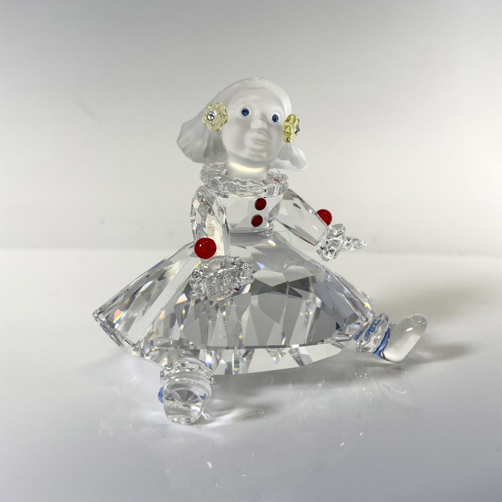 Swarovski Crystal Figurine, Doll: Part of the Cheerful Times collection this adorable figure is sitting dressed in clear crystal dress with red crystal buttons and yellow crystals in her hair, looking out with blue crystal eyes. Swaro