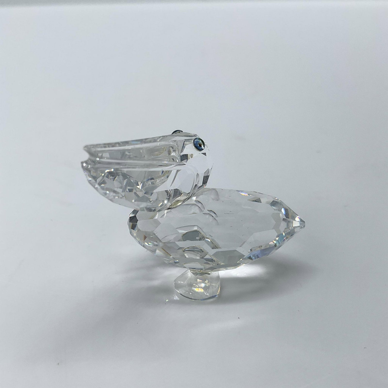 Swarovski Crystal Figurine, Pelican: Introduced for the Feathered Friends theme group this bird features a clear faceted body with blue green eyes. Includes the original box, dimensions: 2.5"H x 3.5"dia. Swarovski etched backstamp. Artis