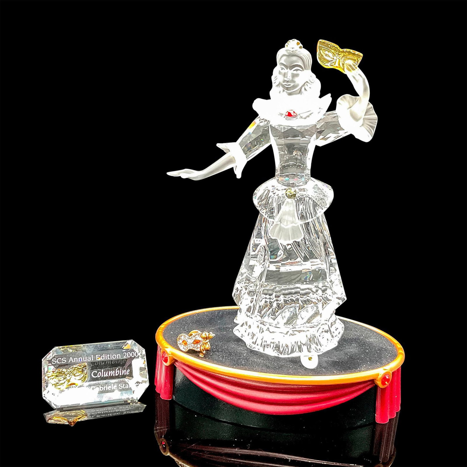Swarovski Crystal Figurine, Plaque & Pin, Columbine 2000: Second piece of the Masquerade trilogy. Clear crystal figural has frosted accents on face, collar, sleeves, dress and shoes, holding a yellow crystal mask. Crown and collar adorned with colored crysta