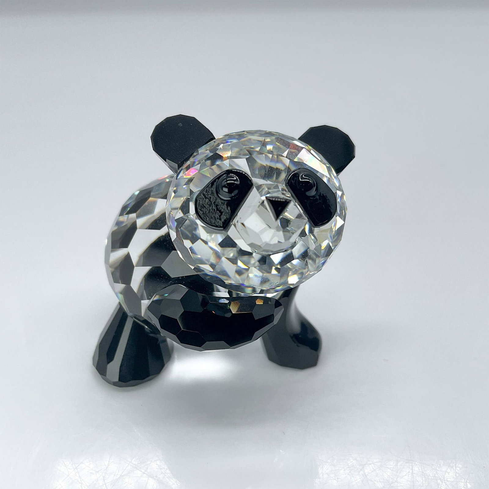 Swarovski Crystal Figurines, Panda Mother: A clear crystal figure of a panda with one arm raised up, with black crystal used for the limbs, ears, and eyes. Swarovski backstamp. Includes Swarovski box: 4.25"H x 4.25"W x 3.25"H. Artist: Adi Stoc
