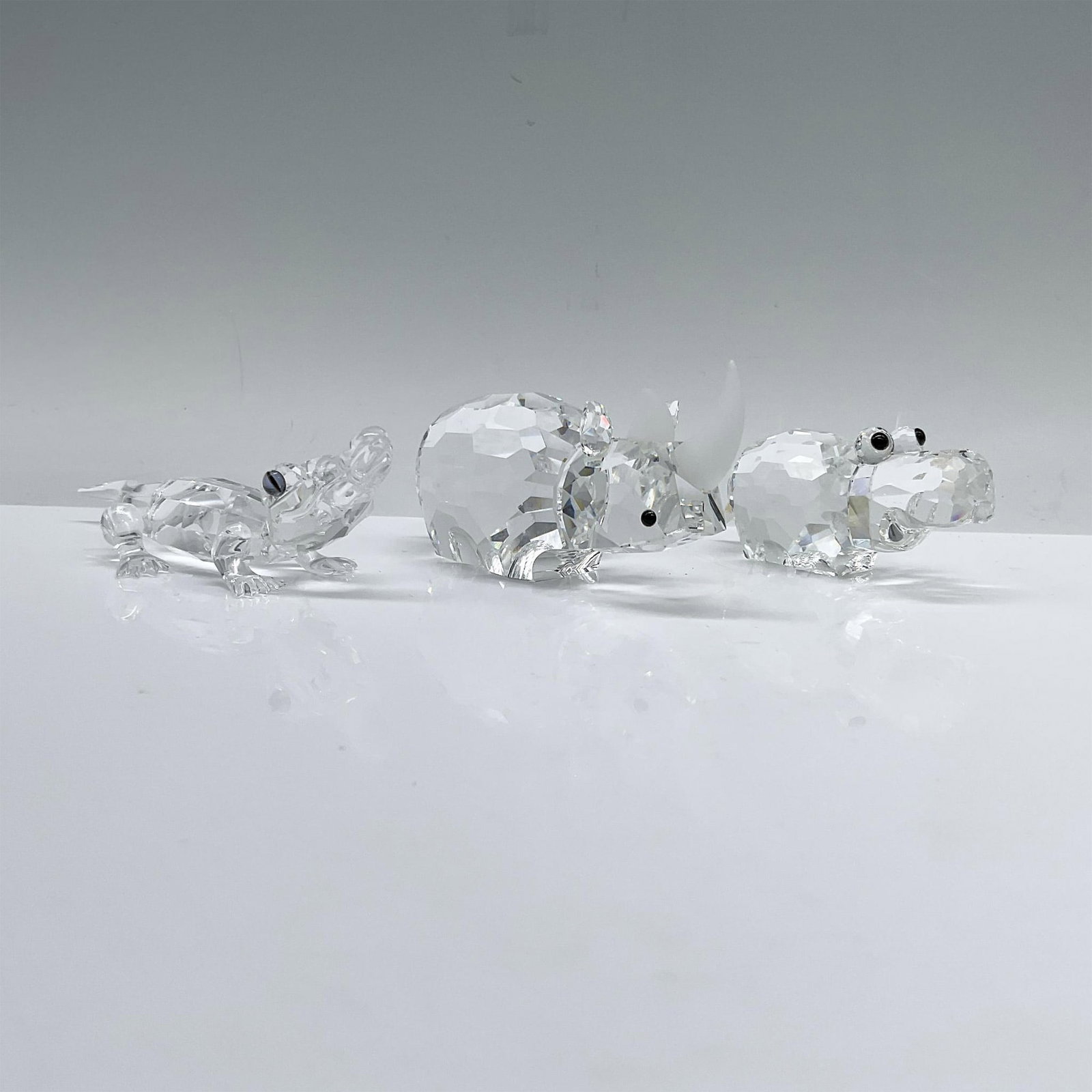3pc Swarovski Wildlife Themed Crystal Figurines: A sturdy rhino (151521) and hippo (151737) standing resolute with piercing black eyes, and a curious alligator (221629) with a raised head, its melon-colored eyes shining. Swarovski backstamp. Dimensi