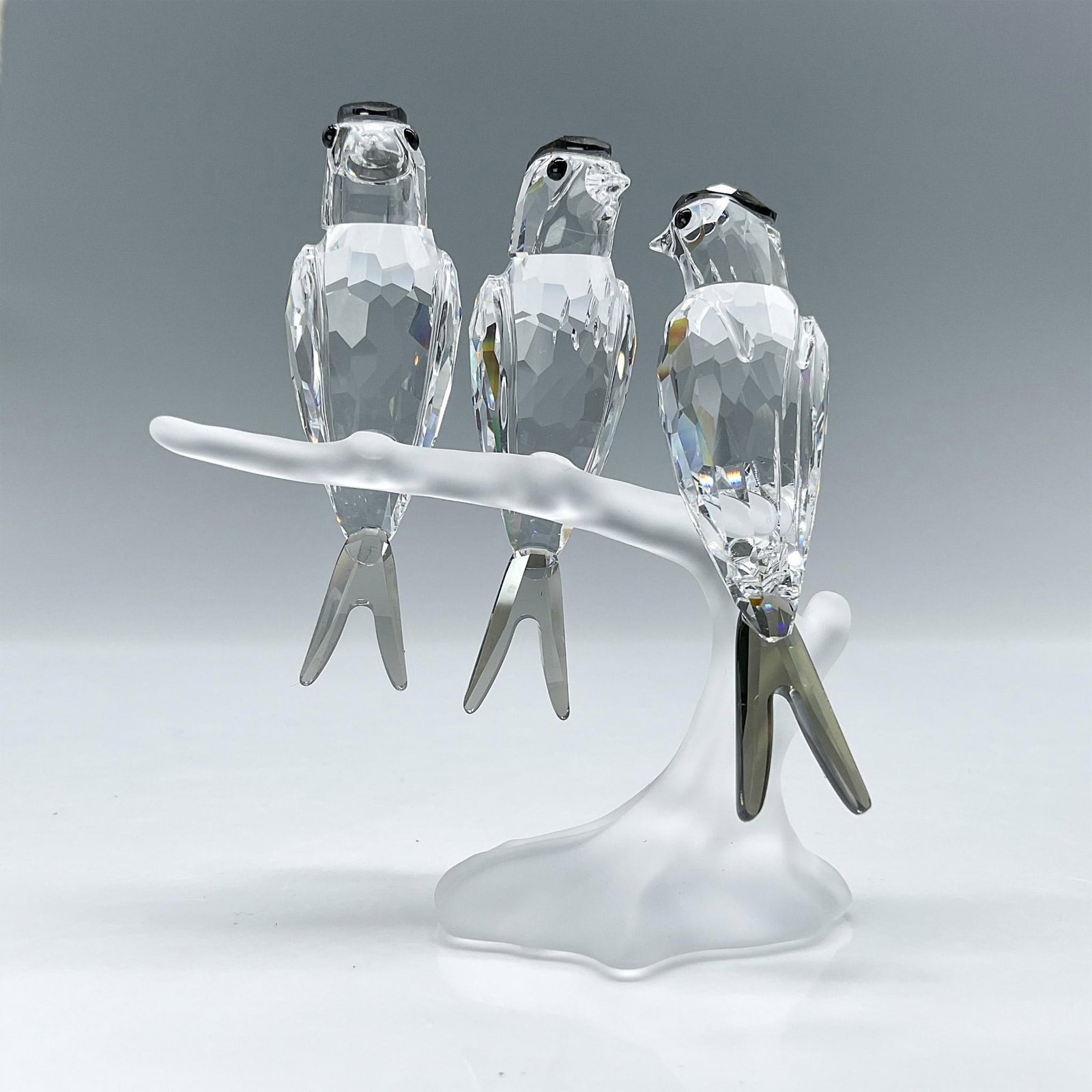 Swarovski Crystal Figurine, Swallows: Three clear faceted crystal birds with black diamond stain crystal head and tail feathers. Perched on a frosted branch. Swarovski backstamp. This item has its original box: 6"L x 6.5"W x 4"H. Artist: 