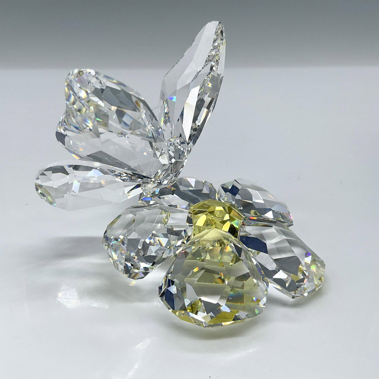 Swarovski Crystal Figurine, Butterfly on Flower 840190: This figurine is made from clear faceted crystal, and the flower has a Jonquil (light yellow) center. Swarovski acid backstamp. This item has its original box measures 6"L x 6"W x 4"H. Artist: Elke Ku