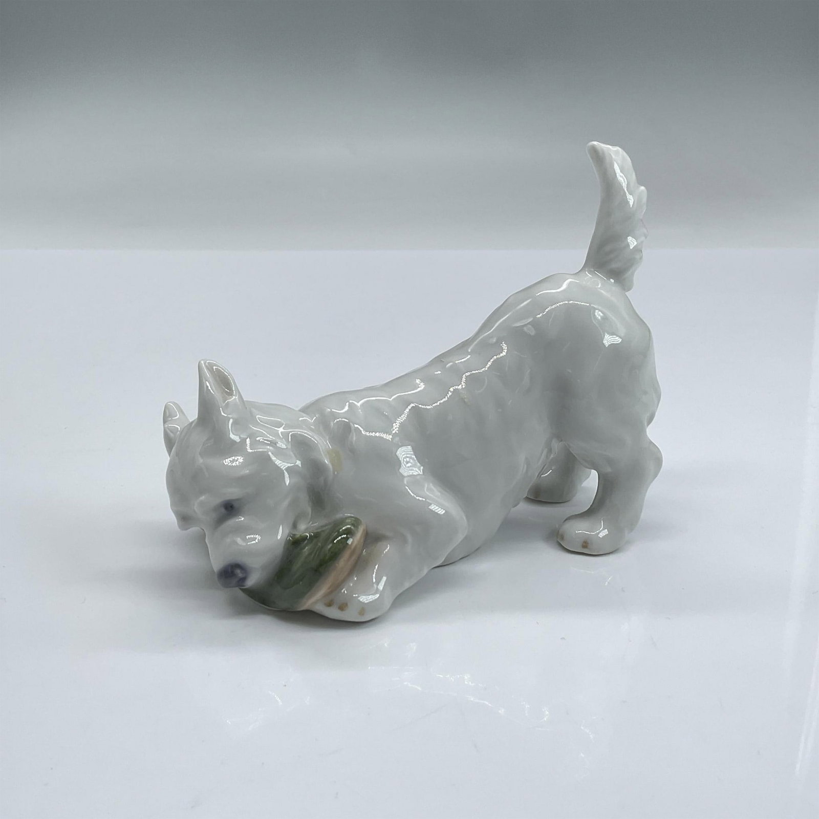 Royal Copenhagen Figurine, West Highland Terrier 3476: Glossy porcelain figure of a white terrier having a great time biting a shoe. Royal Copenhagen backstamp. Dimensions: 4.75"L x 2.25"W x 3.5"H Manufacturer: Royal Copenhagen Country of Origin: Denmark
