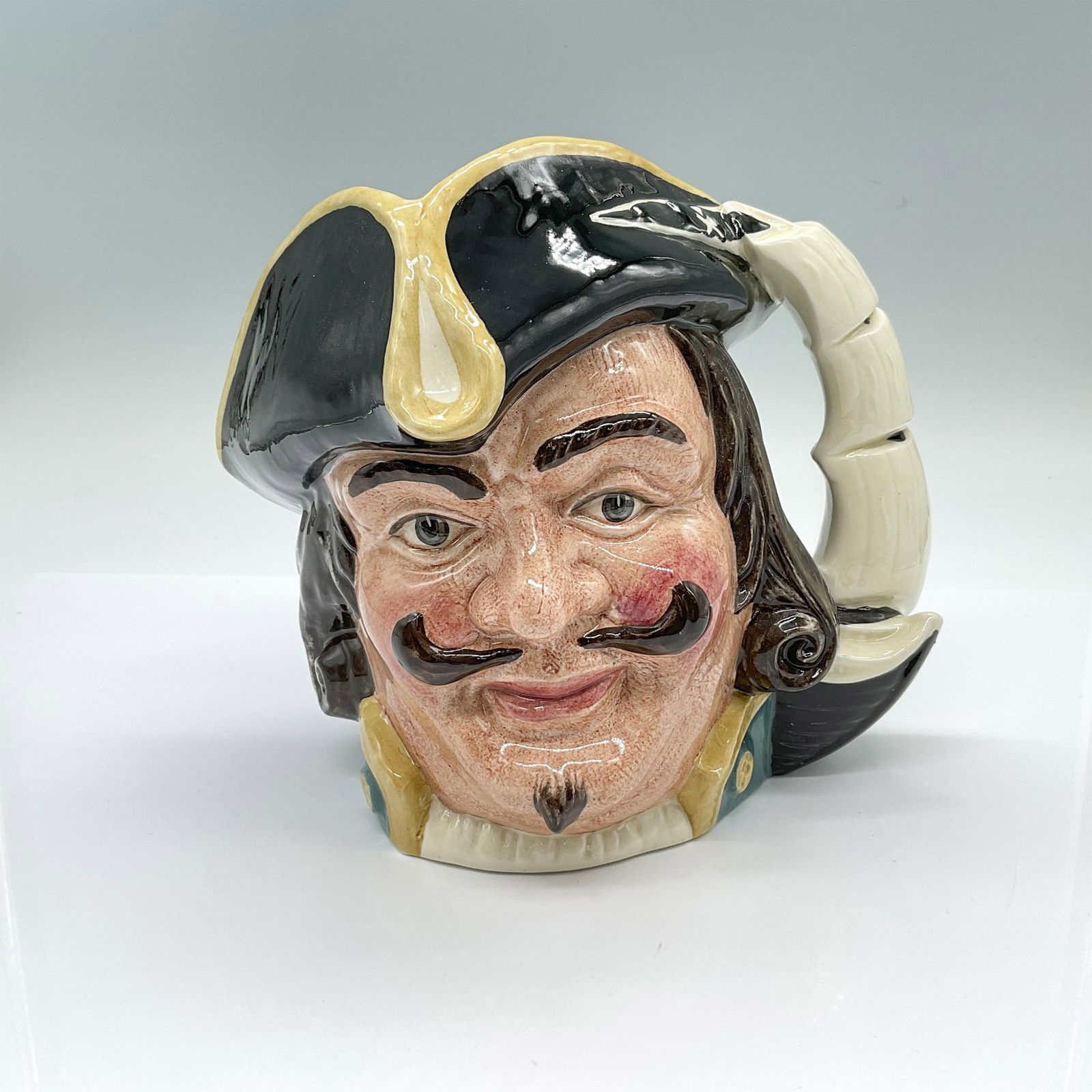 Capt Henry Morgan D6467 - Large - Royal Doulton Character Jug: Hand made and hand decorated glaze figural jug. Blue coat with yellow accents, and a black tricorne with yellow trims. Sails of a ship as the handle. Artist: Garry Sharpe Issued: c. 1958-1982 Dimensio