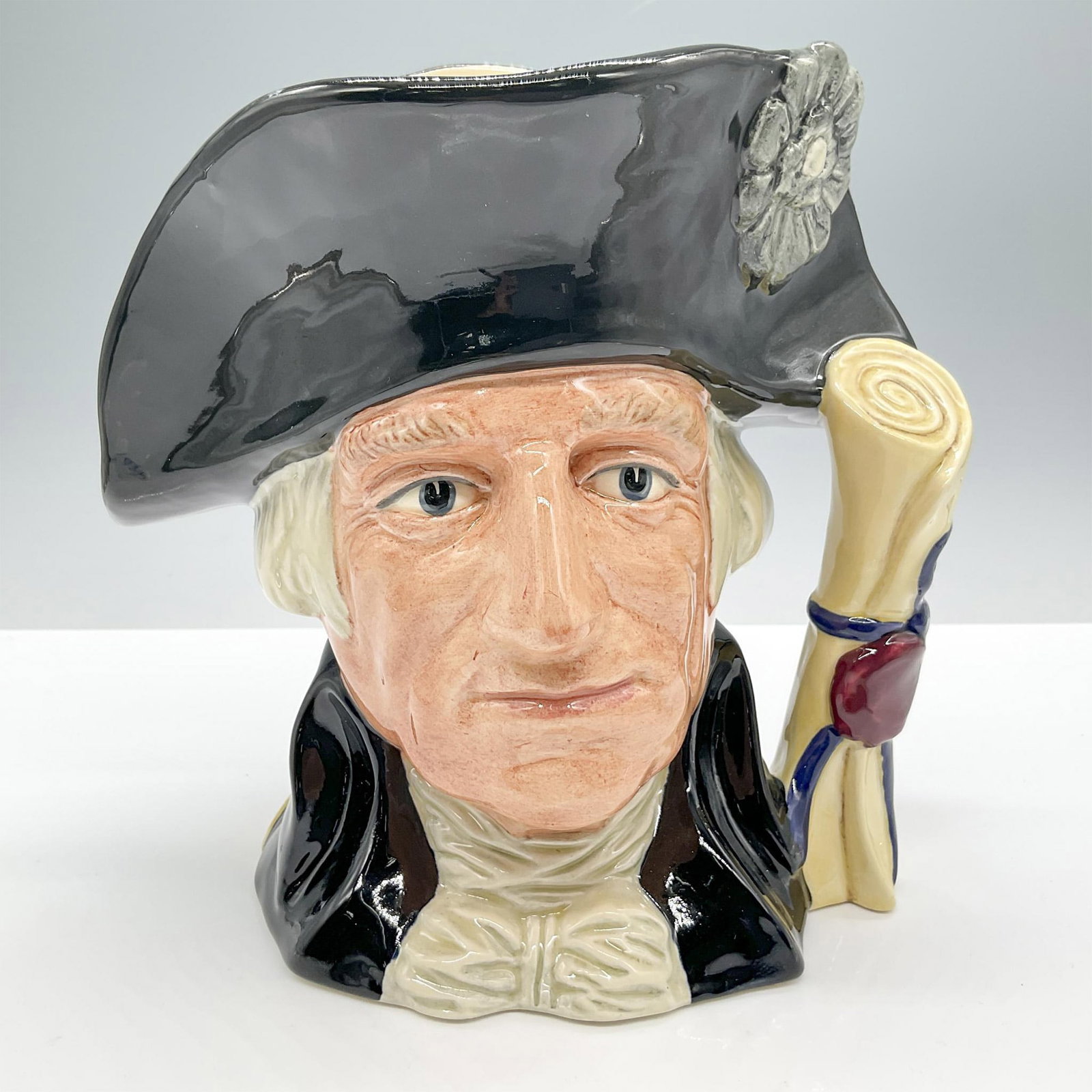 George Washington D6669 - Large - Royal Doulton Character Jug: Style One. Black hat and coat, beige shirt. Royal Doulton backstamp. Artist: Stanley J. Taylor Issued: 1982 - 1994 Dimensions: 7.5"H Manufacturer: Royal Doulton Country of Origin: England