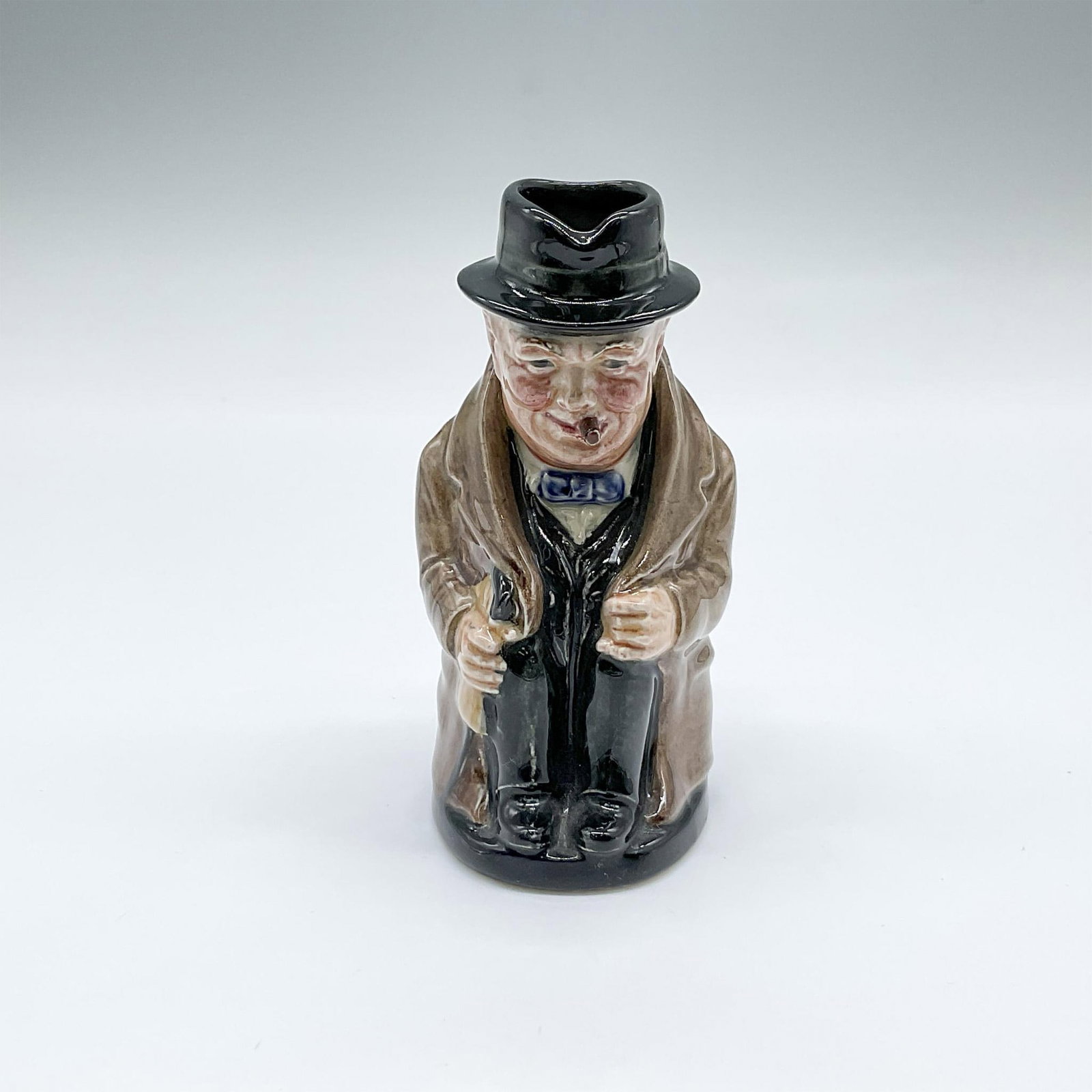 Royal Doulton Small Toby Jug, Winston Churchill D6175: Hand painted and hand modeled seated figural jug of the former Prime Minister of the U.K, smoking a cigar. Plain black handle. Black, blue, and light brown coloration. Artist: Harry Fenton Issued: c 1