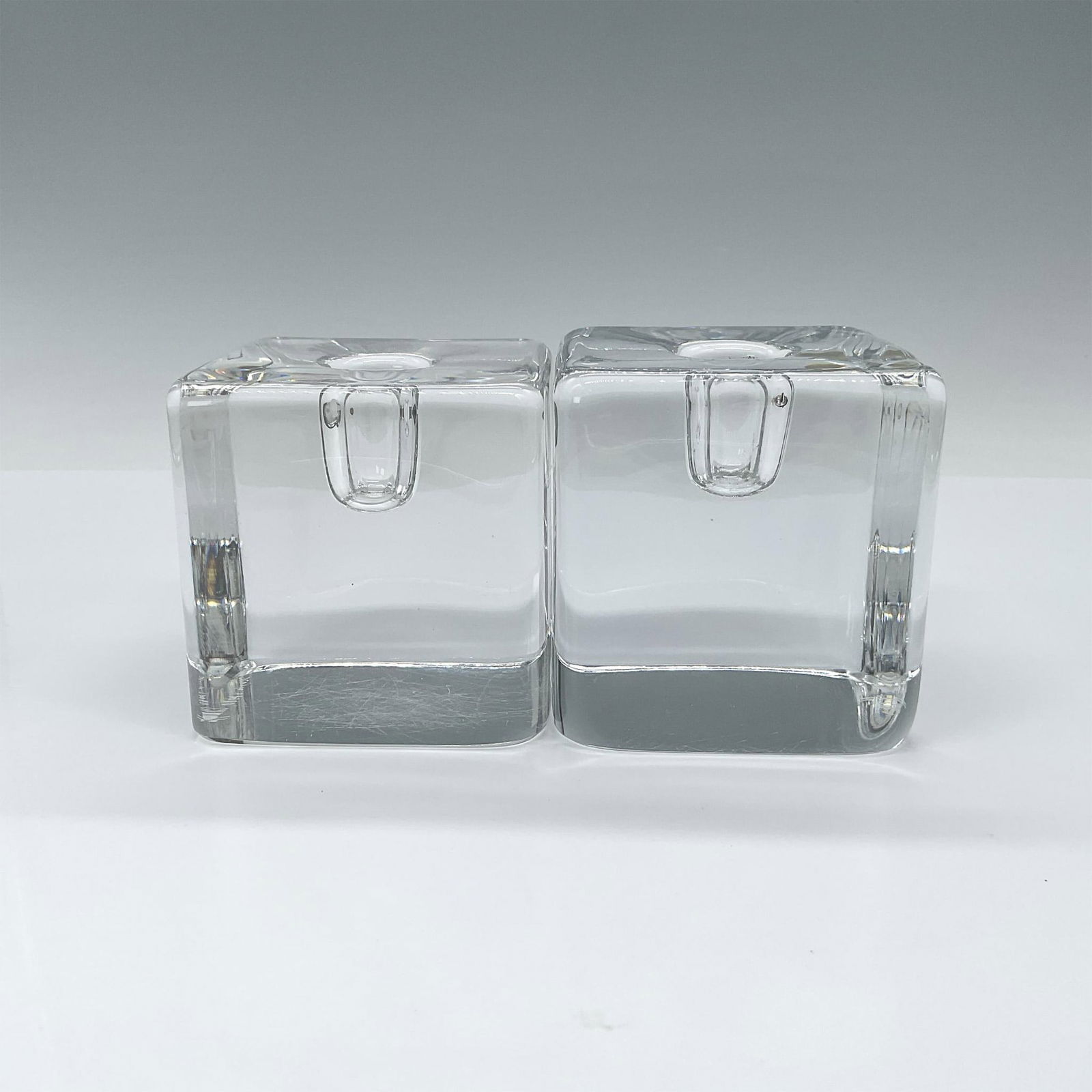 Pair of Kosta Boda Crystal Candle Holders, Cubes 67980: Two matching Solid crystal cube shaped candle holders. Etched signed to base Kosta 67980 Goran Warff. Artist: Goran Warff Dimensions: 3"L x 3"W x3 "H Manufacturer: Kosta Boda Country of Origin: Sweden