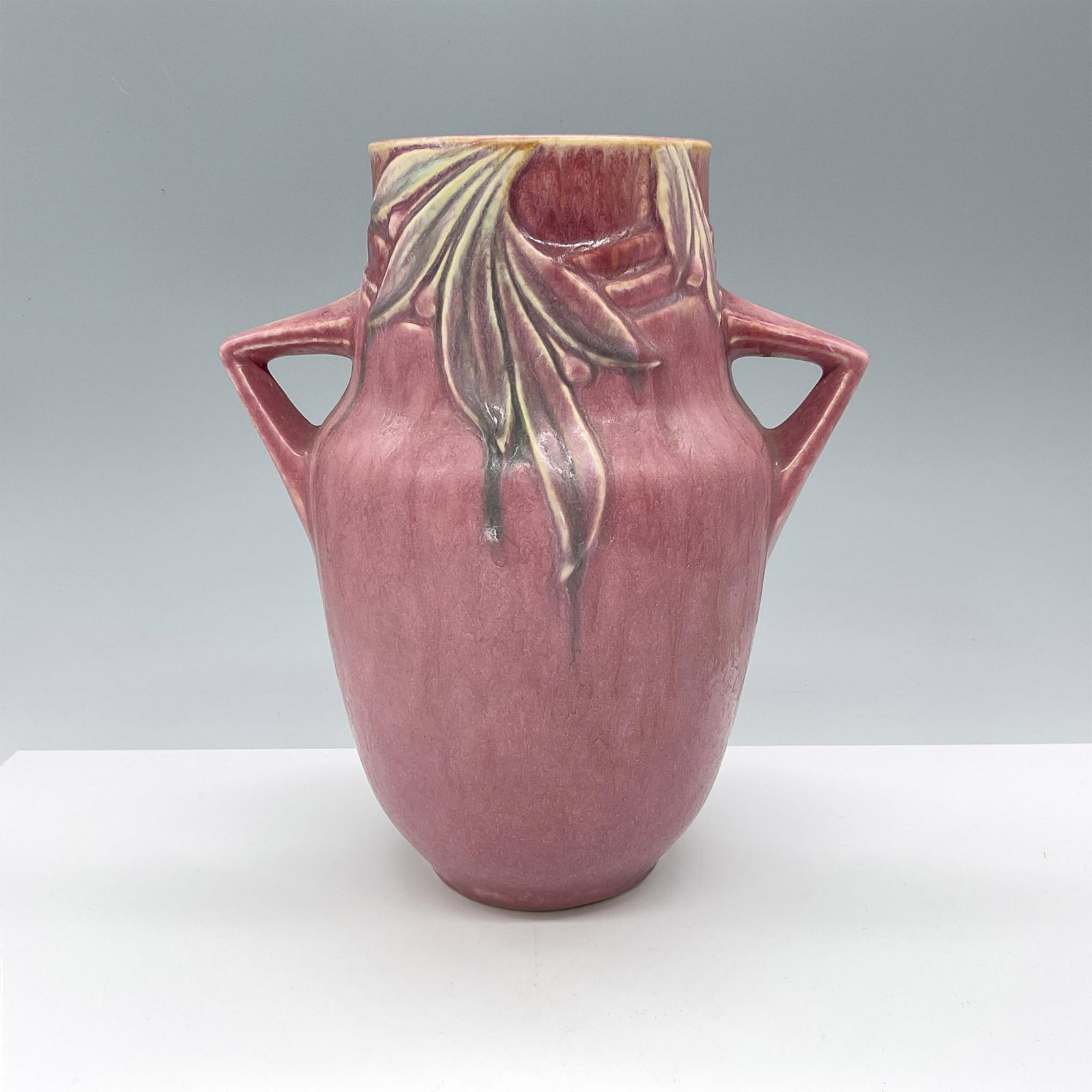 Roseville Art Pottery Pink Velmoss Vase: Dark pink background amphora-shaped bowl with two squared-off handles and decorated with green leaves. Roseville foil sticker on base. Issued: 20th century Dimensions: 8"L x 5.75"W x 9.5"H Manufacture