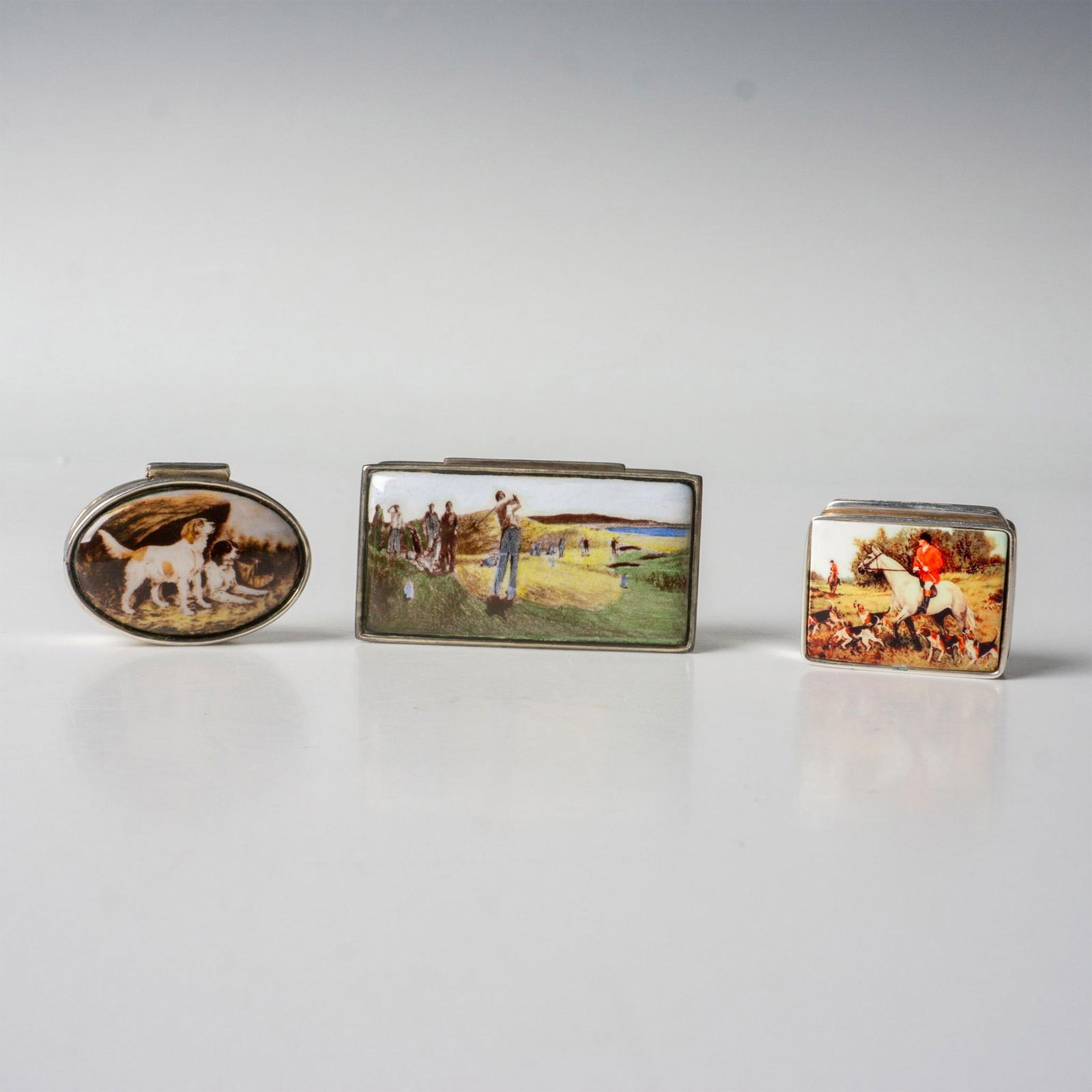 3pc Vintage Painted Porcelain Top Sterling Silver Pillboxes: Three pill boxes marked sterling with images of dogs, a horse and rider in a fox hunt, and a round of golf. The golf box is the largest and measures approximately 2.25"L x 1.25"W x 0.5"H. Dimensions: