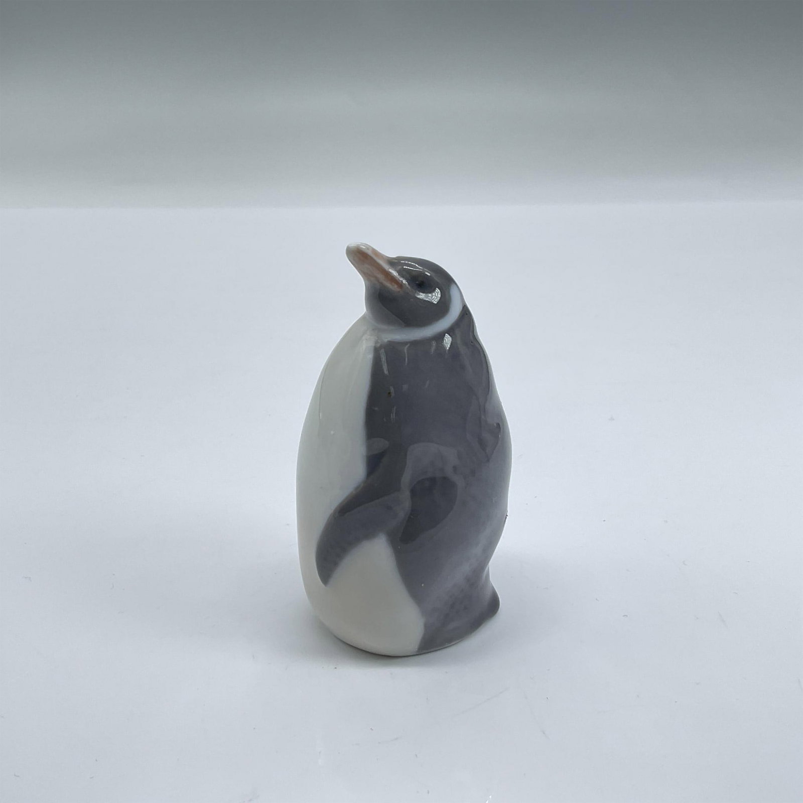 Royal Copenhagen Figurine, Penguin 3003: Porcelain figurine of a grey and white standing penguin. Royal Copenhagen backstamp. Dimensions: 1.5"L x 1.25"W x 2.75"H Manufacturer: Royal Copenhagen Country of Origin: Denmark