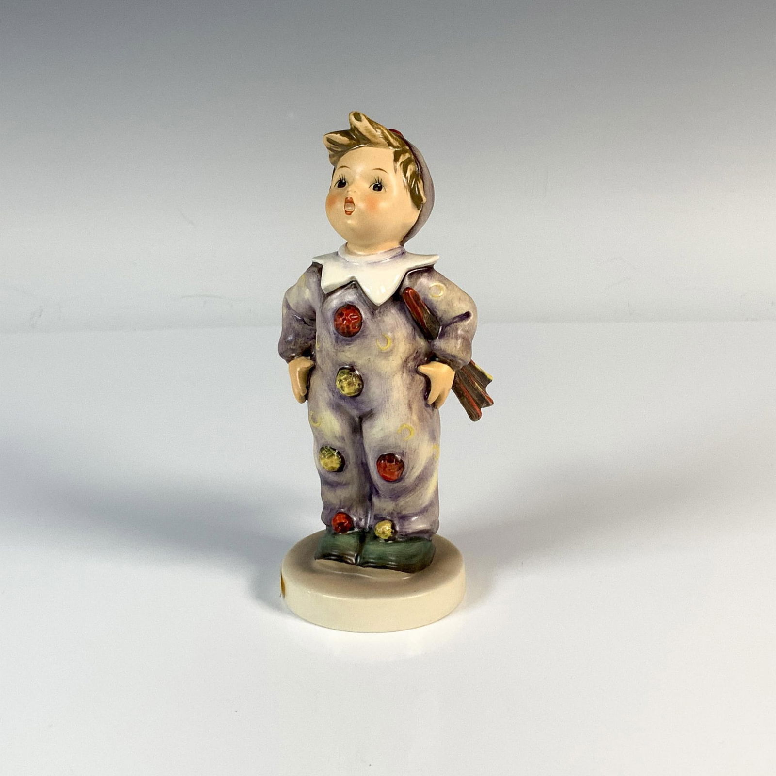 Goebel Hummel Porcelain Figurine, Carnival HUM328: A figure of a boy wearing a colorful clown outfit decorated with moons and pom-poms. M.I. Hummel impressed. Goebel backstamp. Issued: 1957-1999 Dimensions: 2.5"L x 2.75"W x 6"H Manufacturer: Goebel Hu