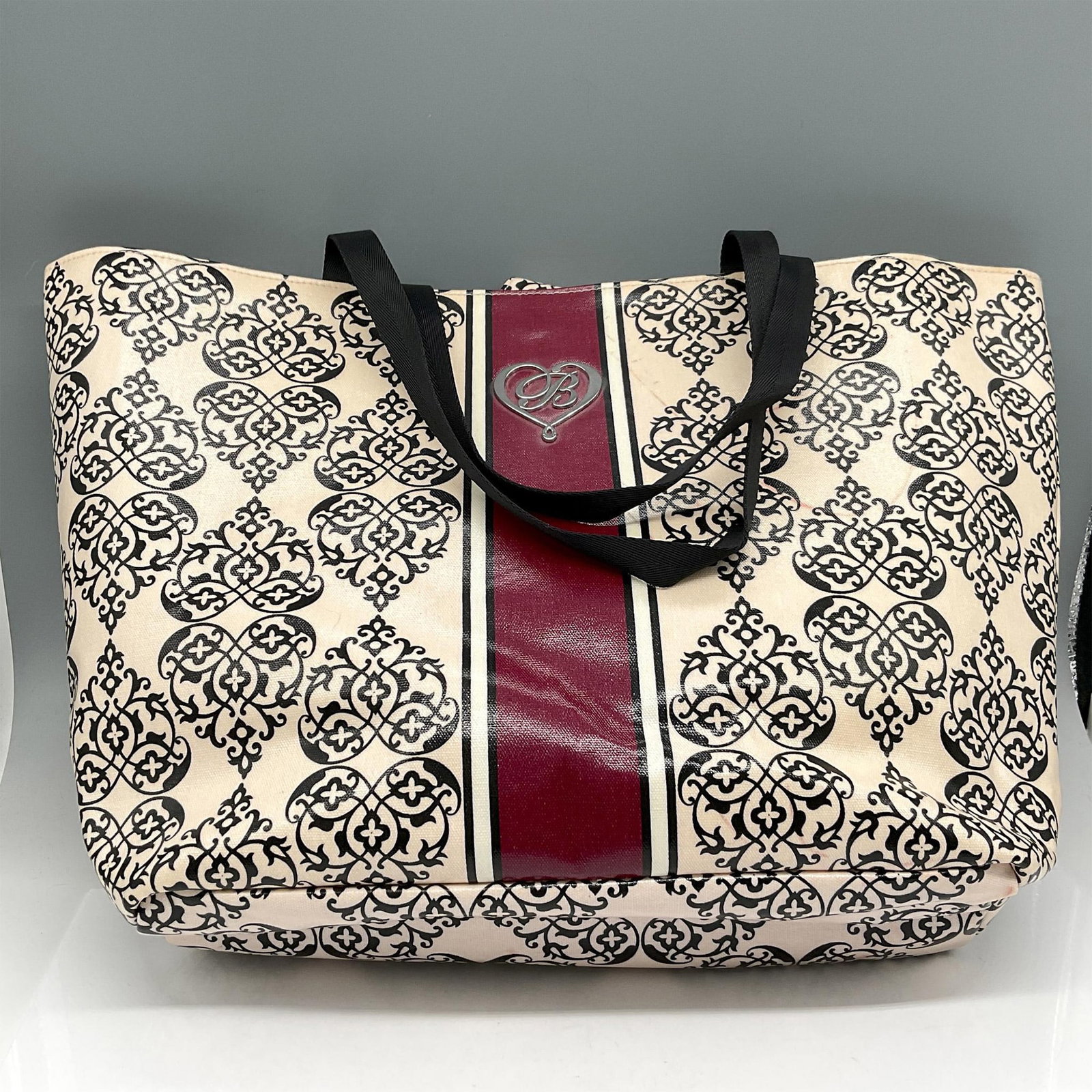 Brighton My Sweet Valentine Carryall Tote Bag: Oversized laminated bag designed in black, cream and red with Brighton logo in heart. Double black canvas strap. Magnetic closure opens to pink striped fabric lining and one zippered pocket. Brighton 