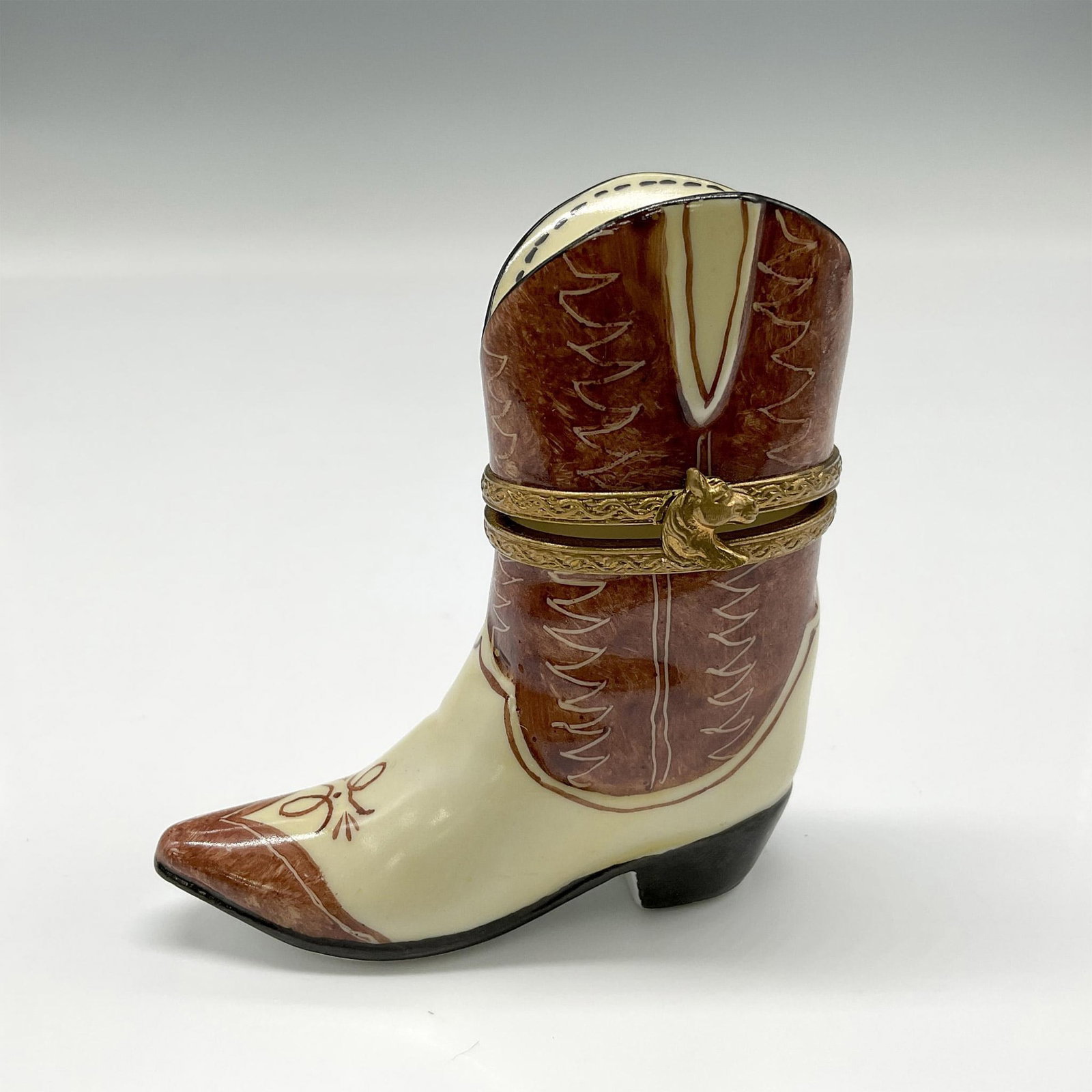 Limoges Peint Main Porcelain Cowboy Boot Box: Tan and cream-colored boot with black heel. Metal hinged banding with horsehead closure. Limoges Peint Main backstamp. Issued: 20th century Dimensions: 1"L x 2.5"W x 3"H Country of Origin: France