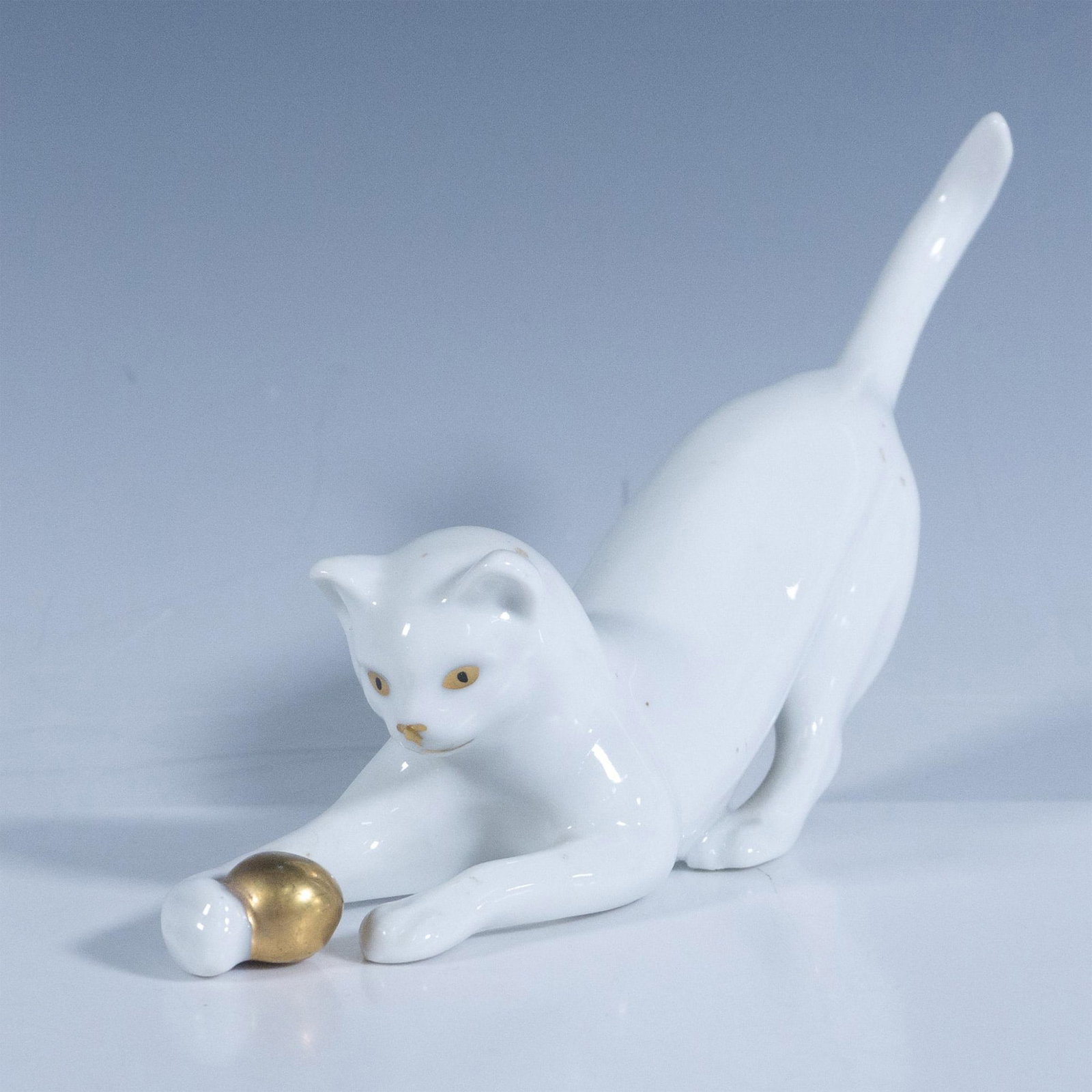 Erphila Porcelain Figurine, White Cat with Ball: White figural with tail up, paws out to catch gilt colored ball. Eyes are black with gilt accent. Erphila Germany backstamp. Issued: 20th century Dimensions: 7"L x 1.5"W x 4"H Manufacturer: Erphila Co