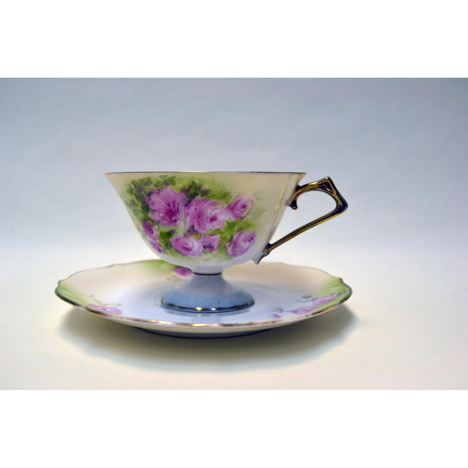 RS Prussia Porcelain Cup And Saucer: Glazed Porcelain Decorated, hand created and hand painted, Hallmark: R S Prussia Backstamp. Ivory Ground with Pink Roses on Green highlighted areas with Gold Accents. A Cherub is hand painted inside t