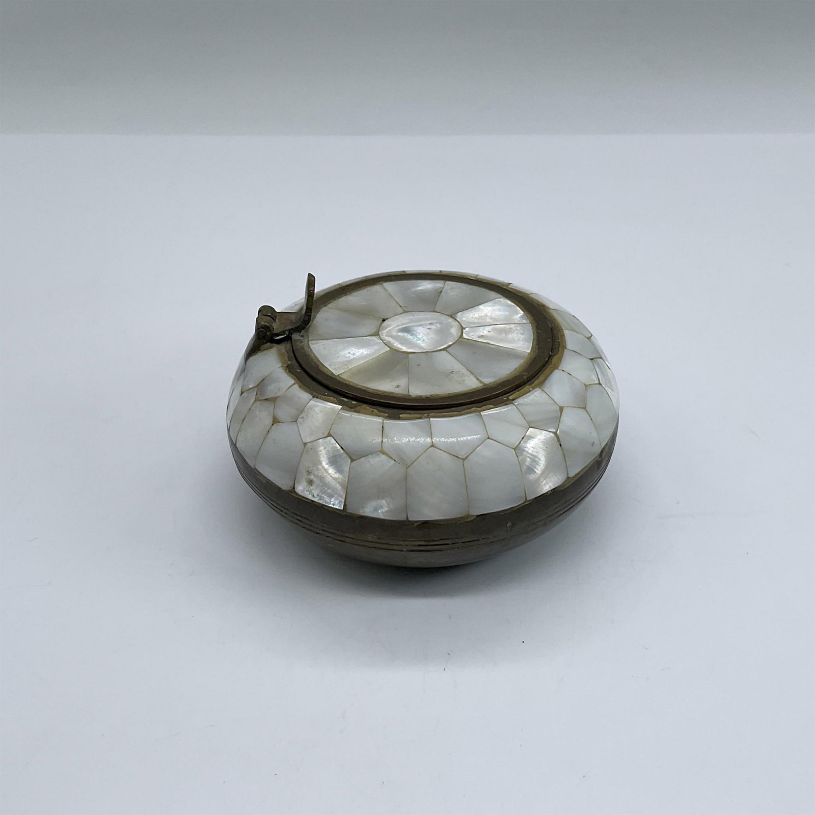 Brass and Mother of Pearl Ashtray: Round brass ashtray decorated with inlaid mother of pearl and a flip top lid. Dimensions: 2"H x 3.5" dia