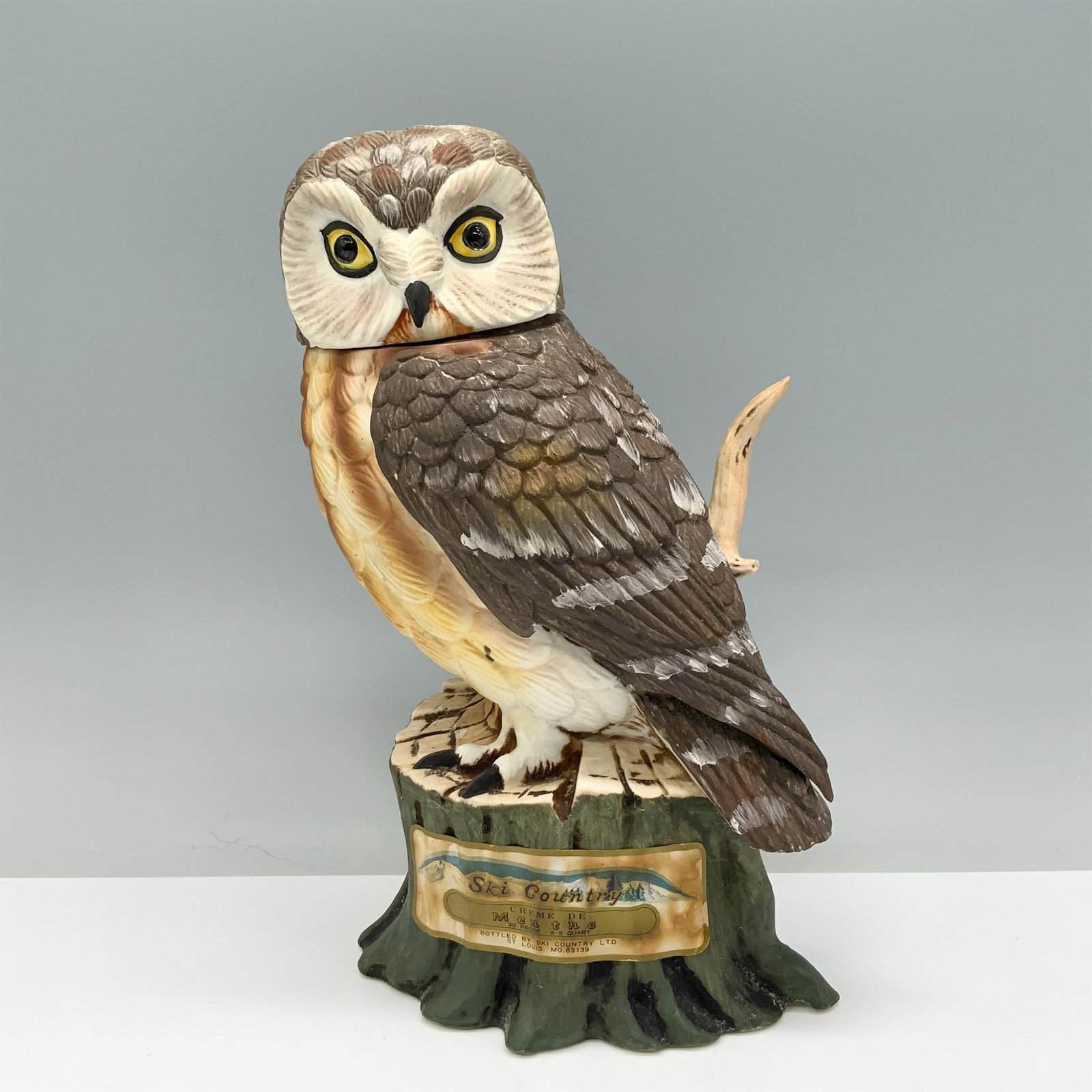 Limited Ed. Foss Company Ski Country Decanter, Saw Whet Owl: A brown, tan, and white owl decanter, standing majestically on a tree stump and gazing attentively to its side. Foss Company backstamp. Ski Country manufacturing sticker. Issued: 1977 Dimensions: 6.5"