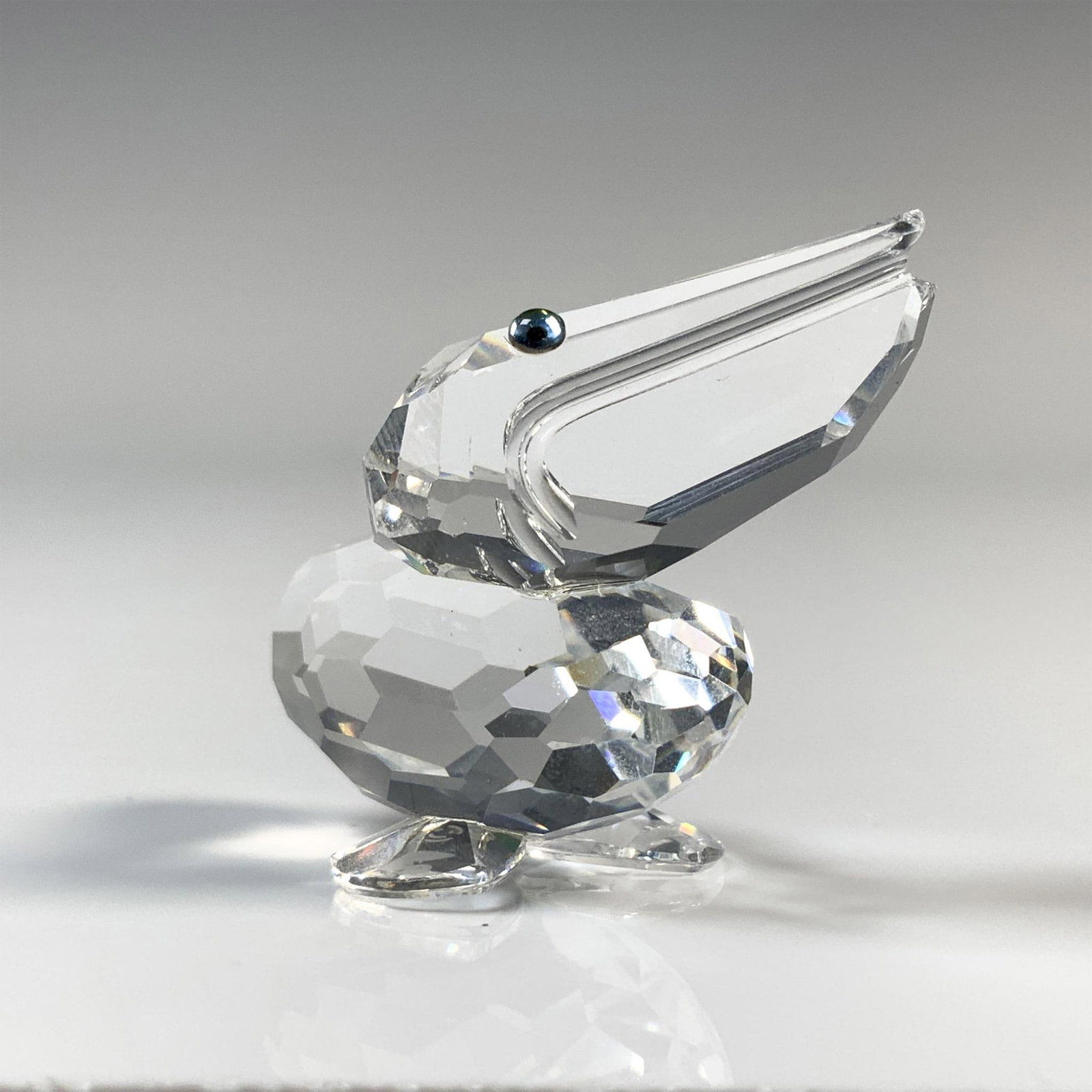 Swarovski Silver Crystal Pelican Figurine, 7679 NR 000 001: Bird is peering upwards with a clear cut crystal body and black eyes. This item has its original box which measures 2.5"H x 3.25" dia. Acid etched Swarovski backstamp. Issued: 20th Century Dimensions: